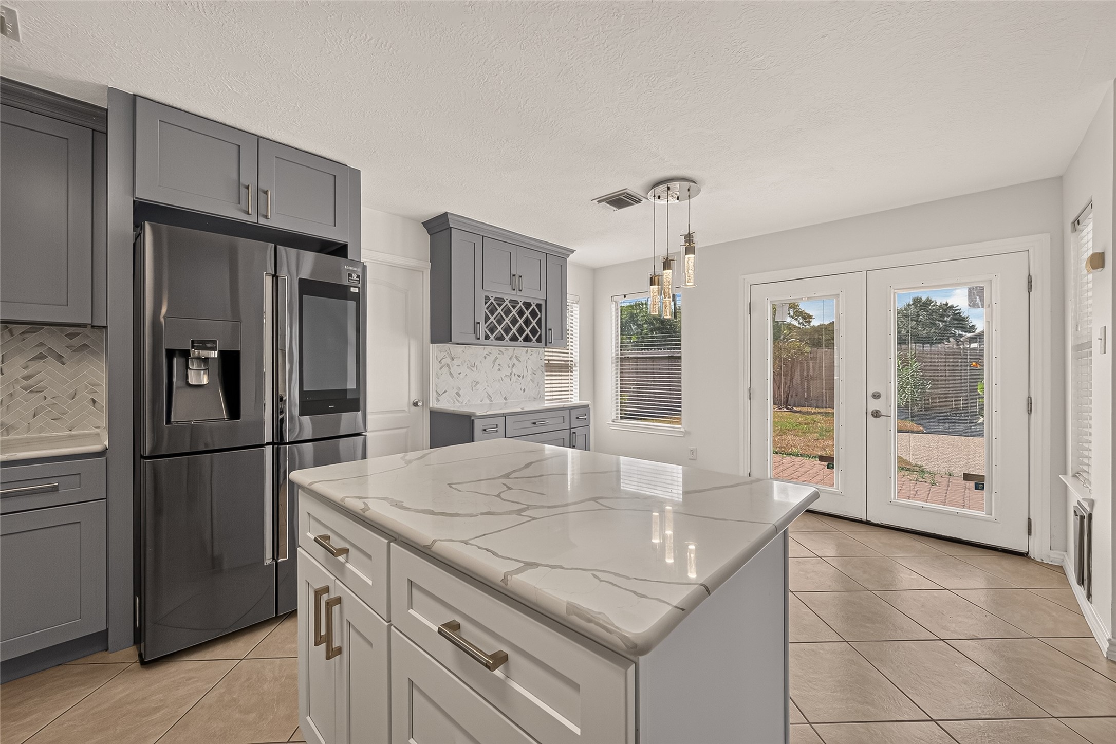 The kitchen island takes center stage in this view, with sweeping quartz countertops, ample prep space, a stainless steel refrigerator, and French doors leading to the backyard.