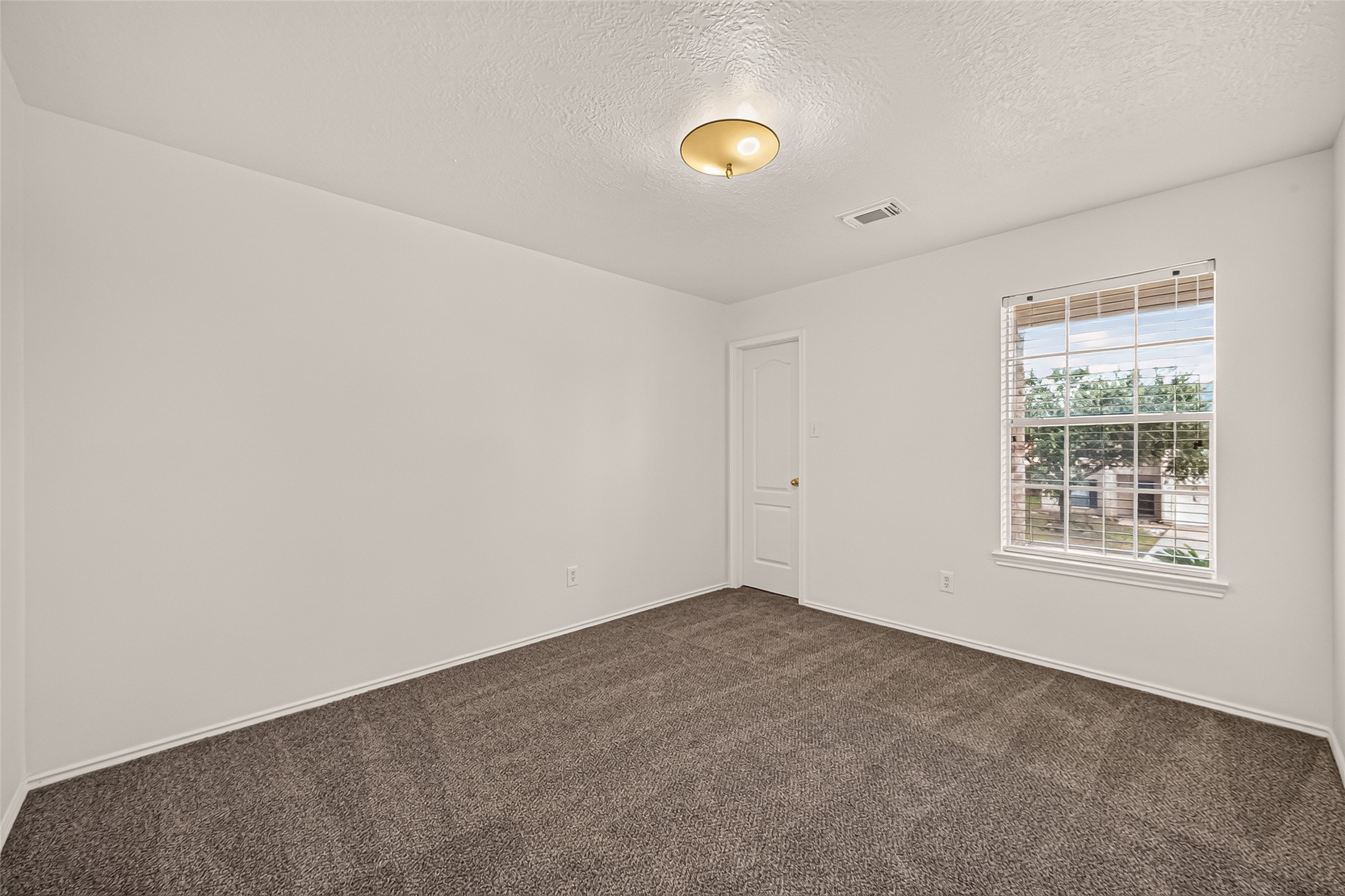 A bright first guest bedroom with soft carpeting, a generous window, and a versatile layout ready to make your own.