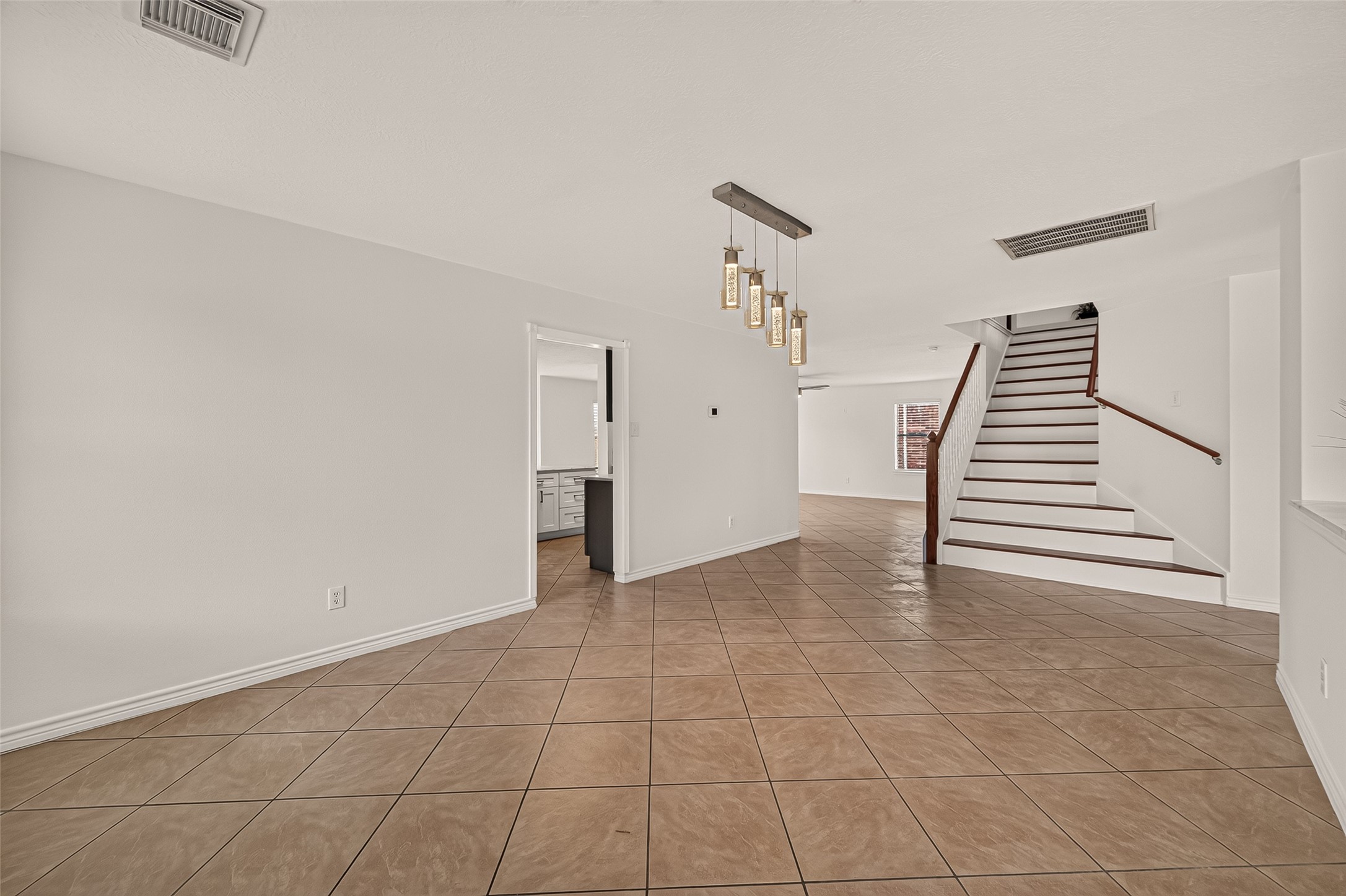 From the dining room, the open layout flows toward the living area, while the pendant lights and staircase add character to the space.