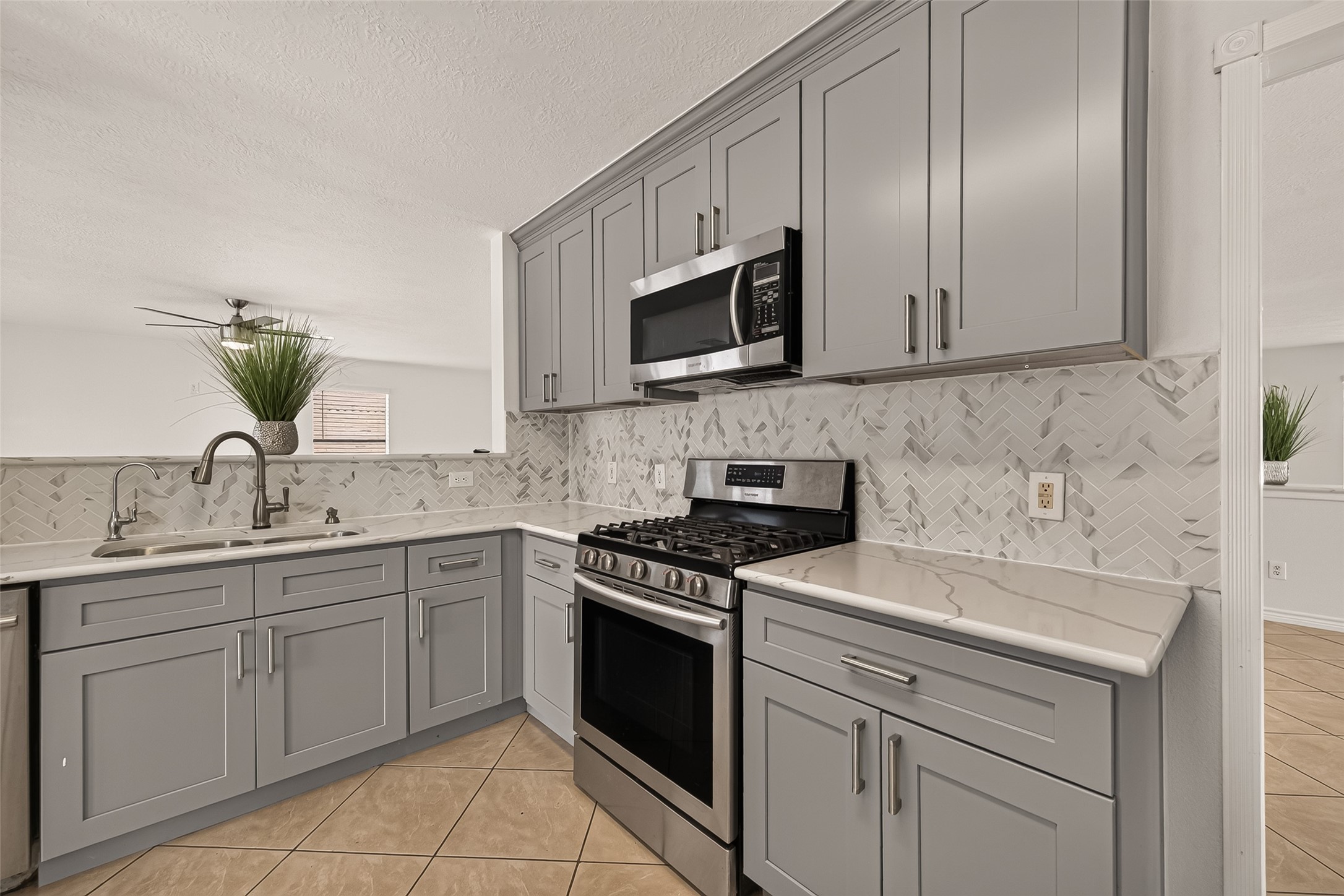 A closer look at the kitchen highlights the gray shaker cabinets, patterned tile backsplash, stainless steel gas range, and generous counter space.