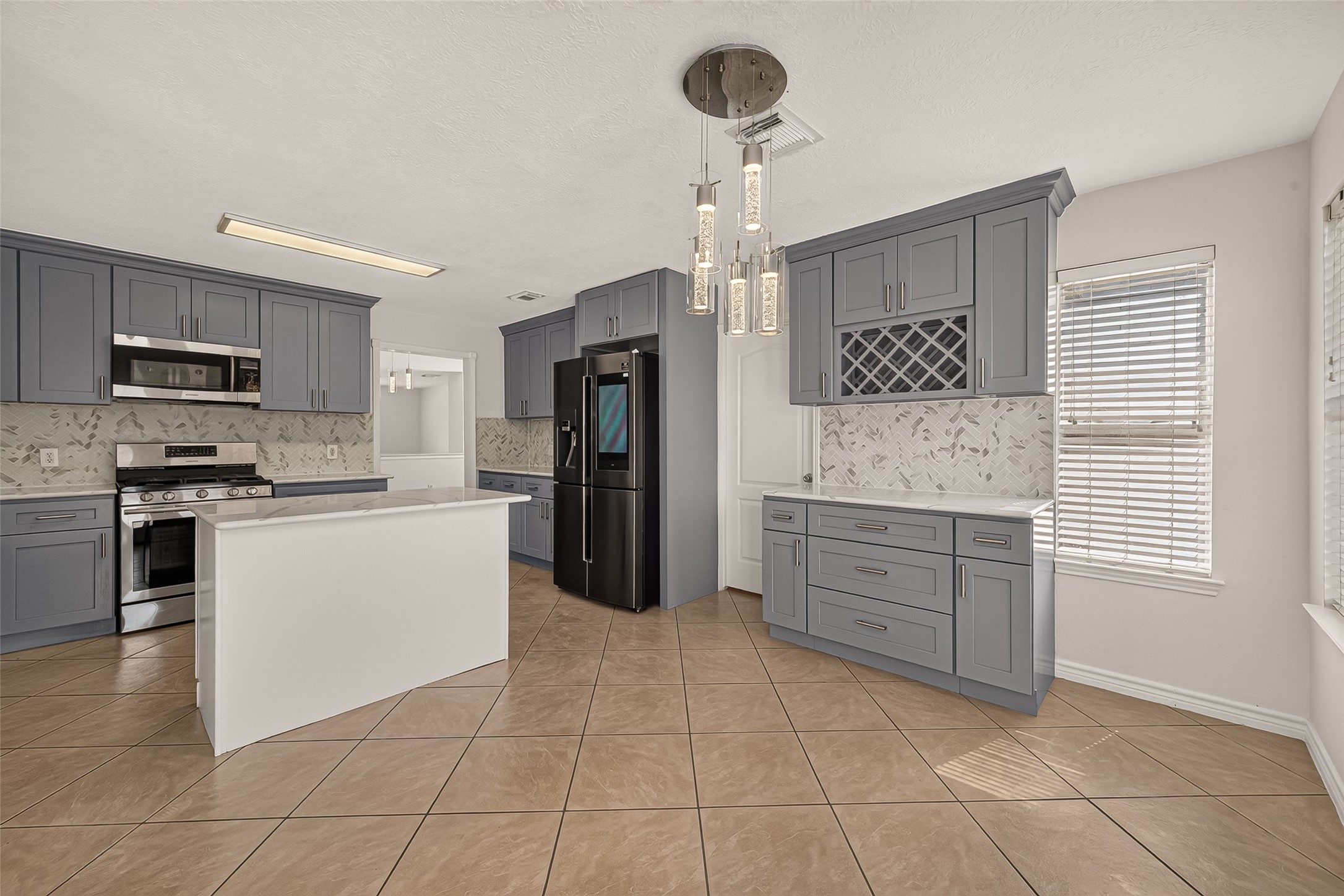 Another angle from the breakfast room of the kitchen, that showcases the dedicated beverage station with a built-in wine rack, pendant lighting over the island, and plenty of cabinetry for storage.