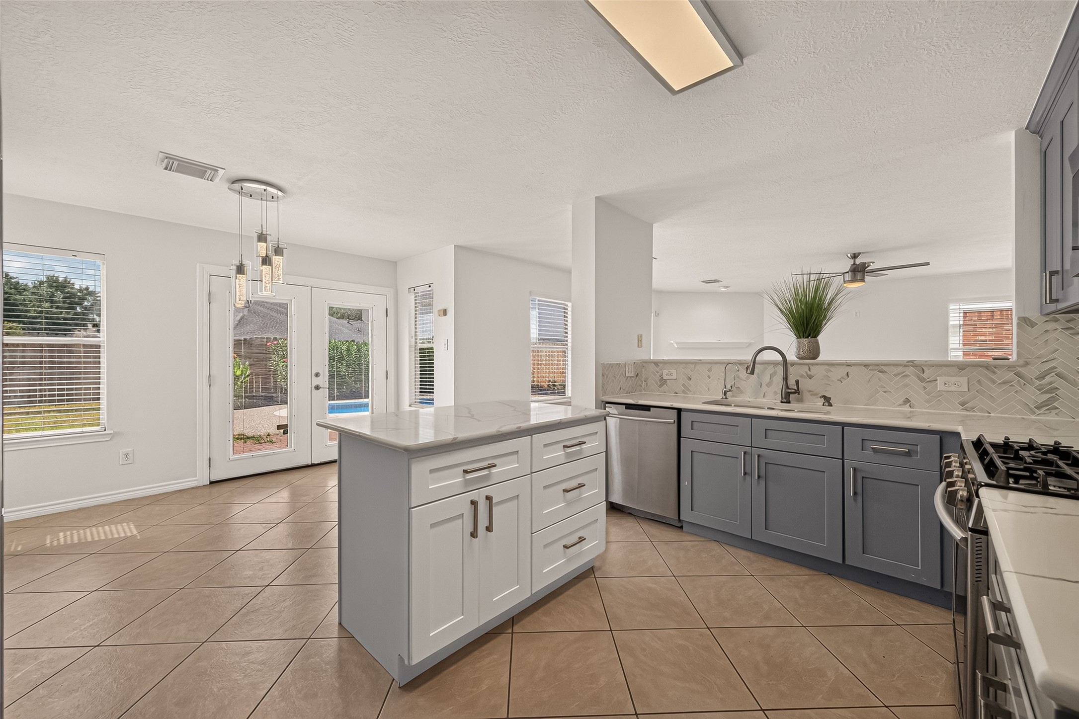 The kitchen brings everyone together with a generous island, two-tone cabinetry, and a view into the family room. French doors nearby open toward the pool for easy indoor-outdoor entertaining.