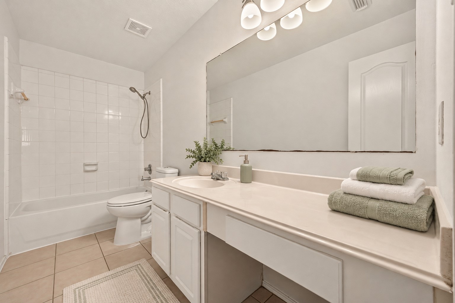 The secondary bathroom offers a tiled tub and shower, a spacious vanity counter, and a bright, clean look. Virtually staged.