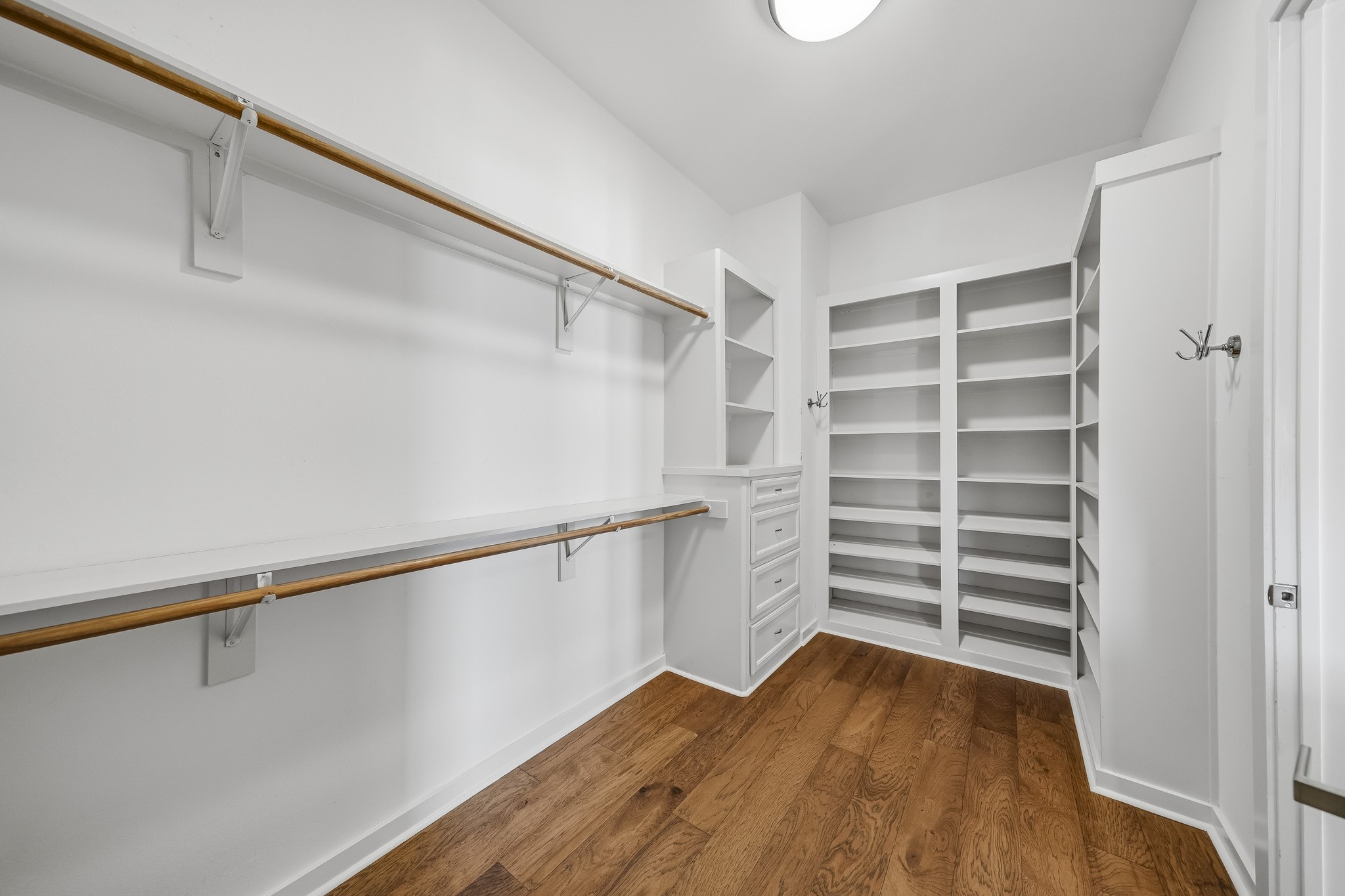 The spacious primary closet offers exceptional wardrobe storage with built-in shelving, convenient drawers, and dual hanging rods with additional shelf space, creating a beautifully organized setting for clothing, shoes, and accessories.