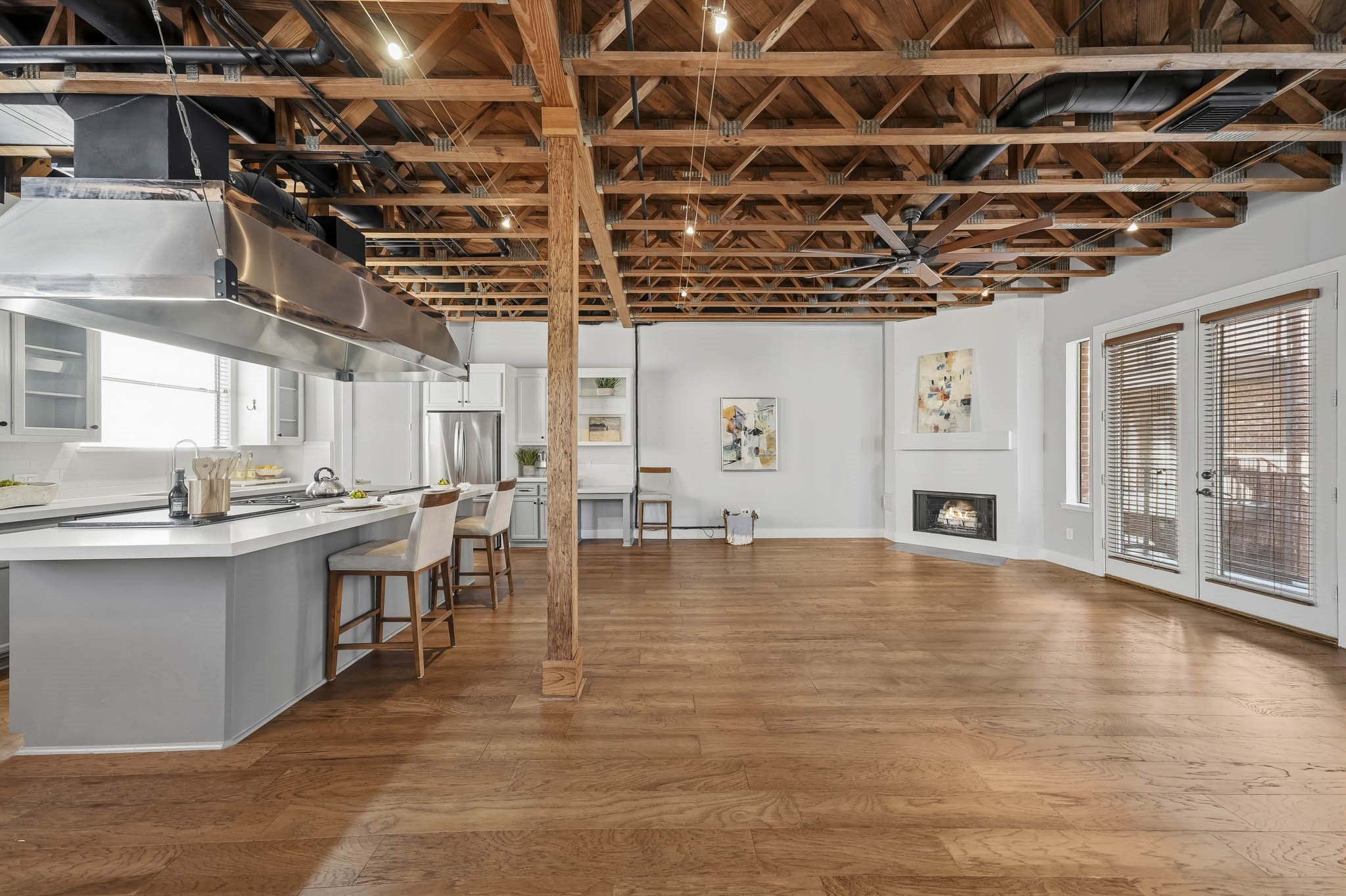 The second-floor family room offers a warm and sophisticated gathering space, featuring rich hardwood floors installed in 2023, architectural exposed beams and distinctive wood trusses that lend timeless character. Track lighting, integrated speakers and a ceiling fan complete this inviting space, blending architectural charm with modern comfort.