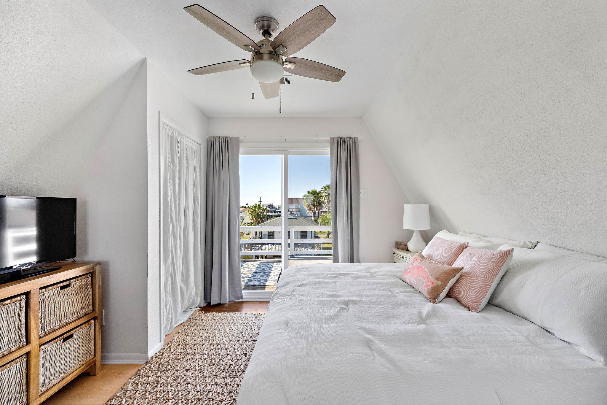 Bright and airy bedroom with a king-sized bed, ceiling fan, and sliding glass doors leading to a private balcony, offering serene views.