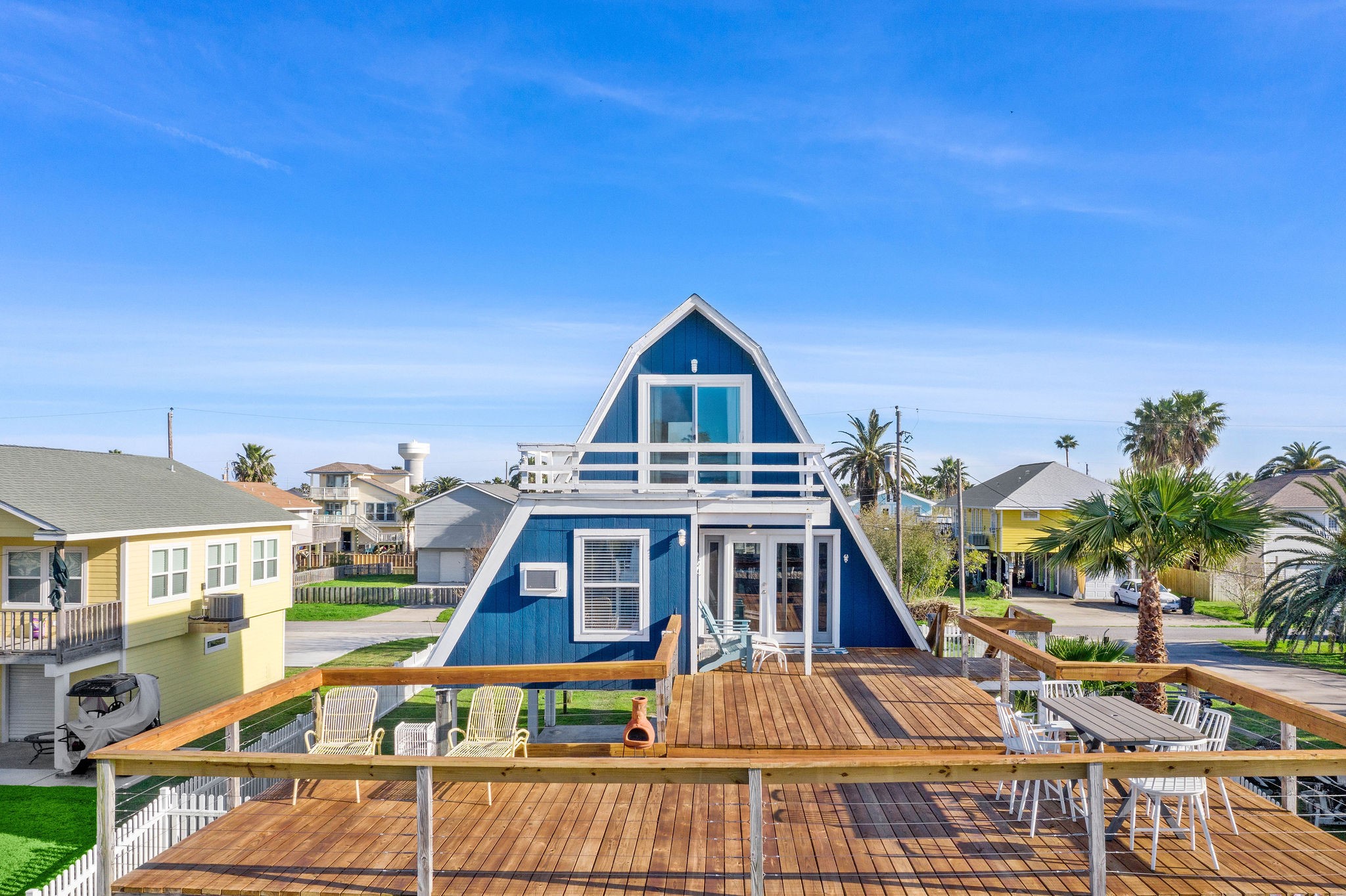 Charming A-frame home with a spacious wooden deck perfect for outdoor entertaining, surrounded by palm trees in a serene neighborhood setting.