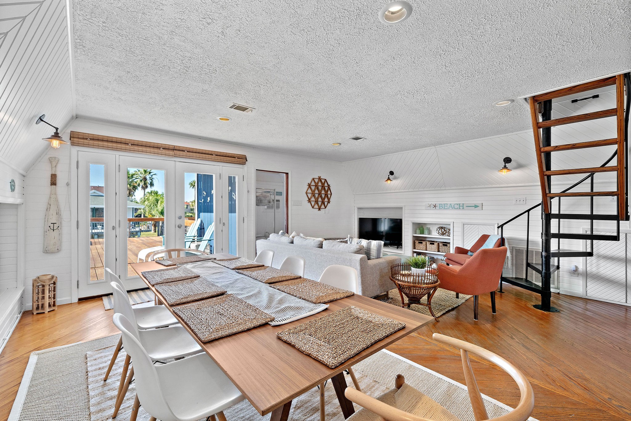 Bright and inviting open-concept living area with a seamless flow from the dining space to a cozy lounge, featuring large French doors that open to a sunlit deck.