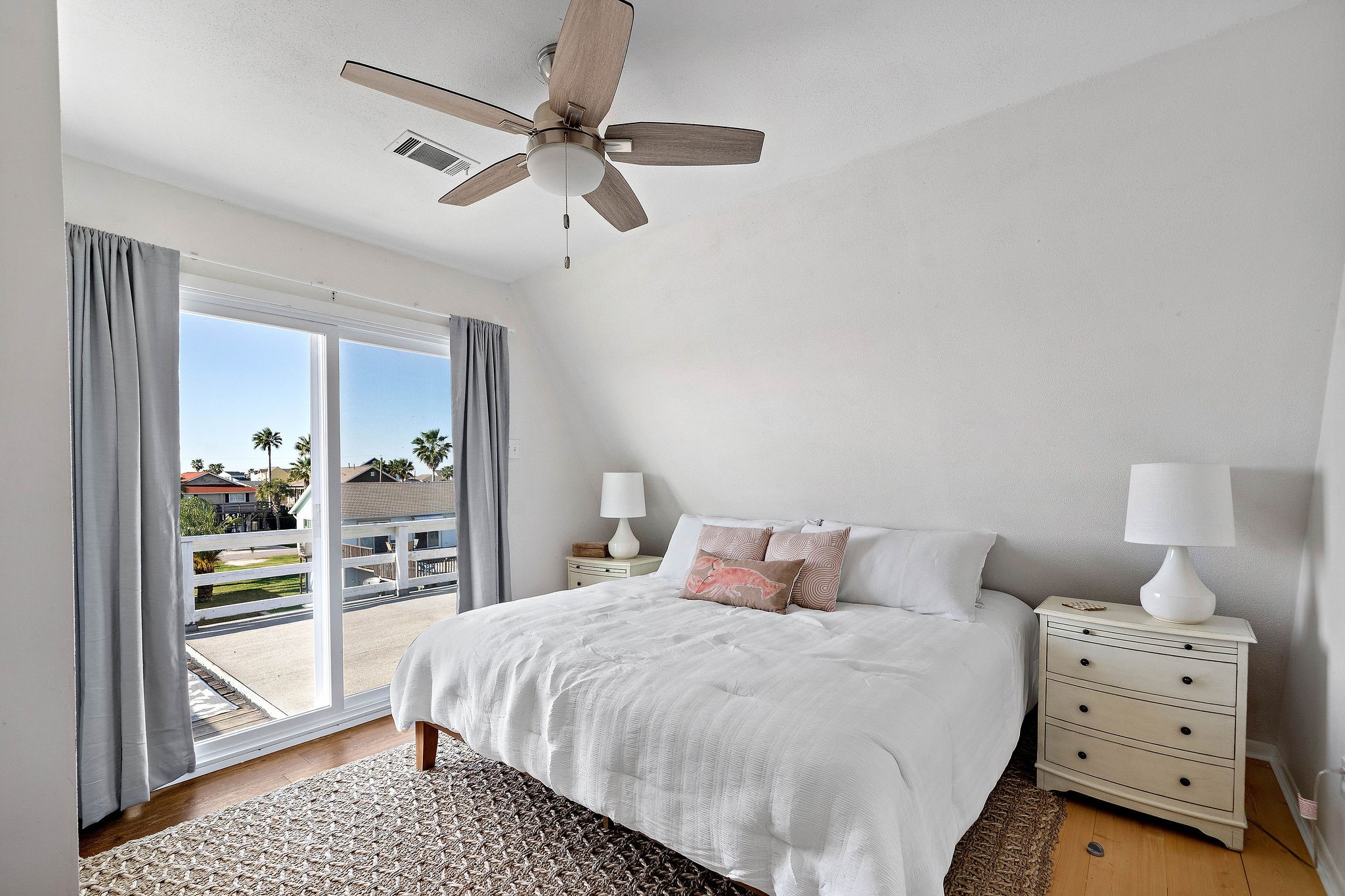 Bright and airy bedroom featuring a large window with scenic views, neutral decor, and a ceiling fan for comfort.