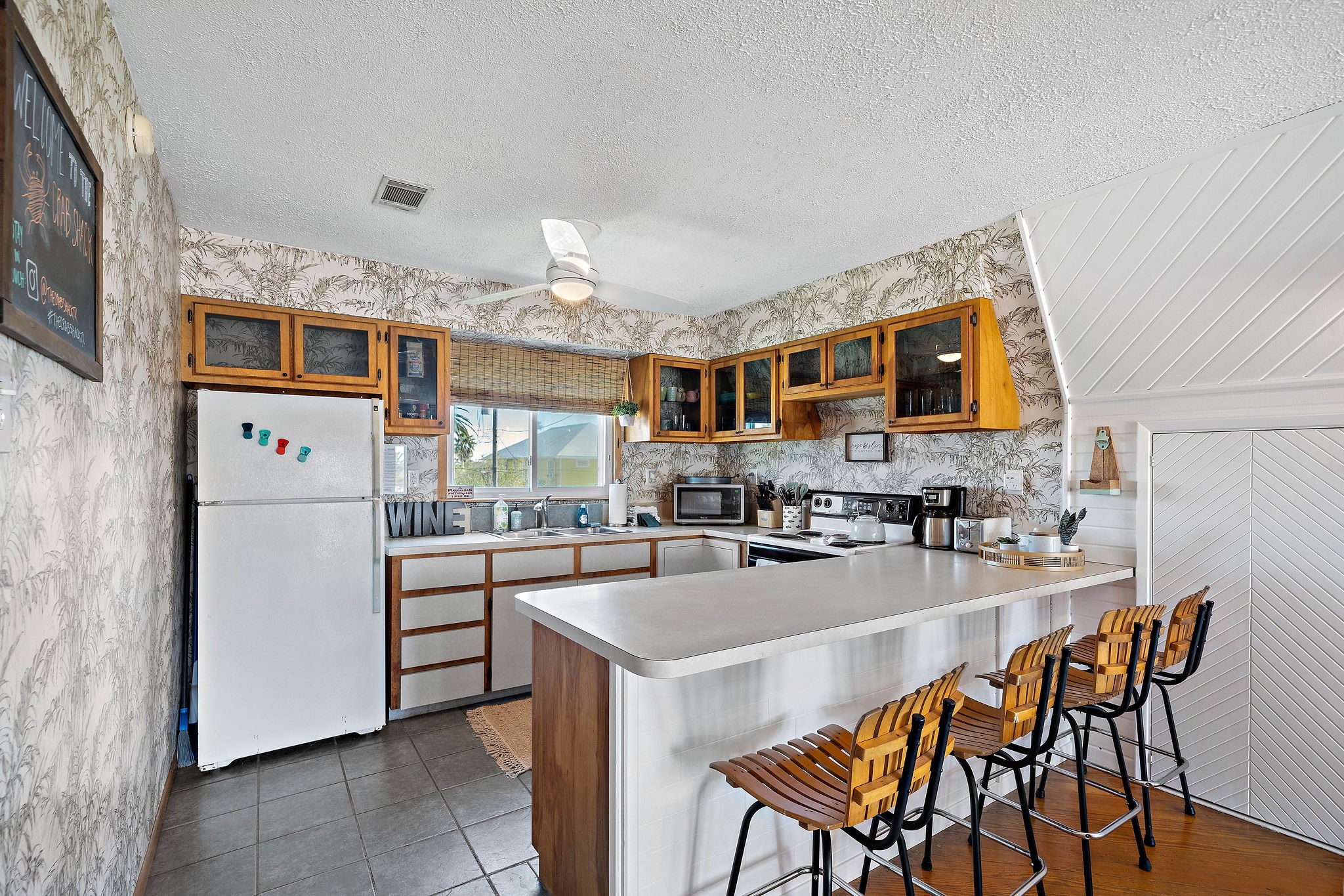 Charming kitchen with rustic wooden cabinetry, a spacious breakfast bar with seating, and modern appliances set against a stylish patterned wallpaper. Charming kitchen with rustic wooden cabinetry, a spacious breakfast bar with seating, and modern appliances set against a stylish patterned wallpaper.
