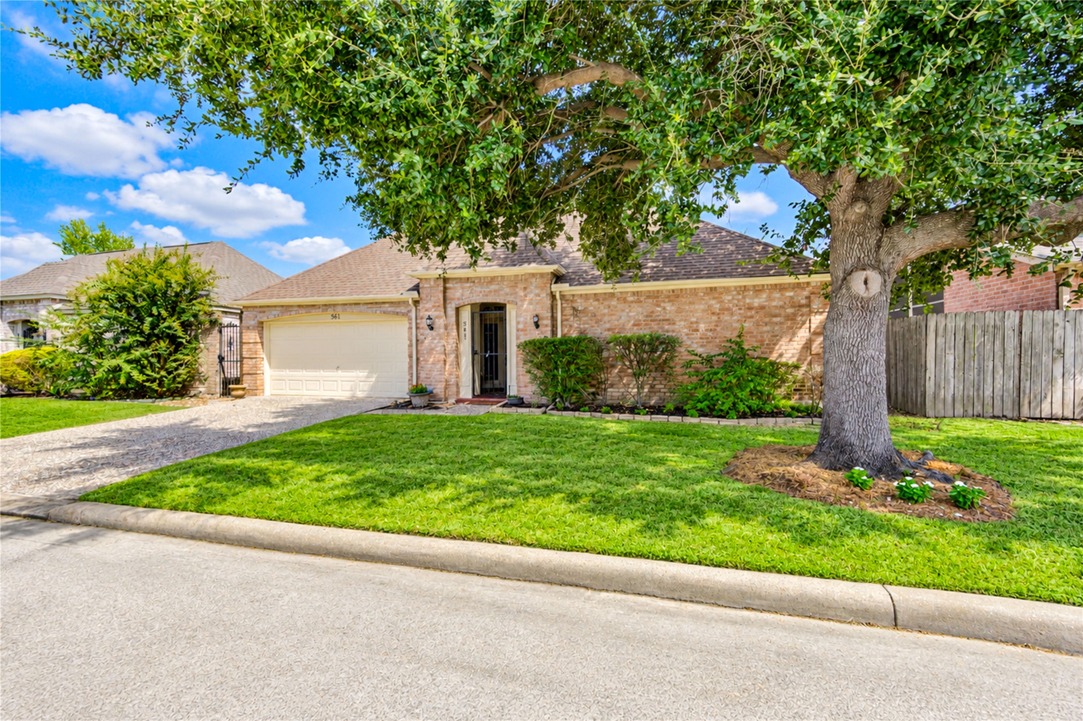 Charming brick home with a spacious front yard and mature tree, offering a welcoming entrance and attached two-car garage.