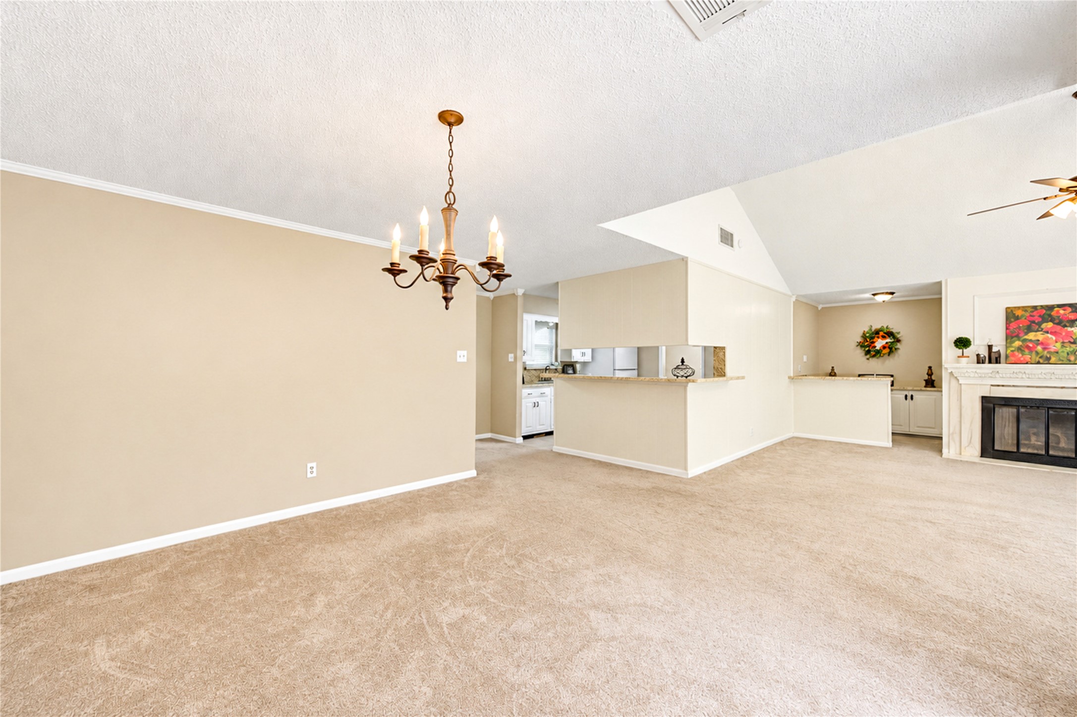 Spacious open-plan living area featuring a cozy fireplace, elegant chandelier, and neutral tones, seamlessly connecting to the kitchen and dining spaces.
