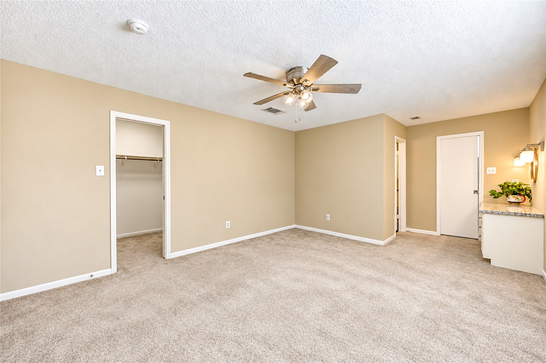 Spacious bedroom with neutral tones, featuring plush carpeting, a ceiling fan, and ample closet space for comfortable living.