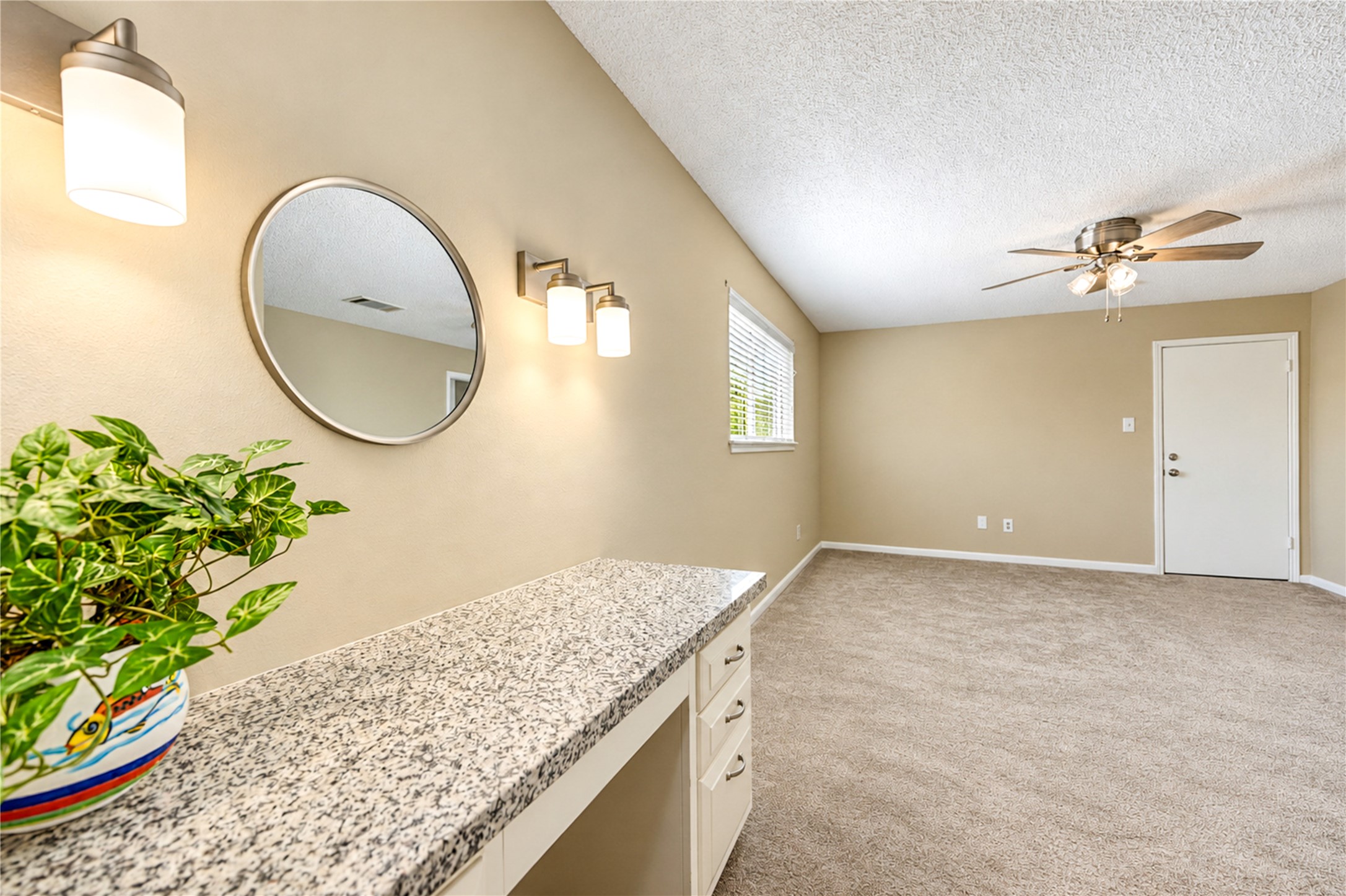 Spacious master bedroom with neutral tones, featuring plush carpeting, a brand new ceiling fan, and abundant natural light. A stylish vanity with a granite countertop and modern lighting adds elegance.