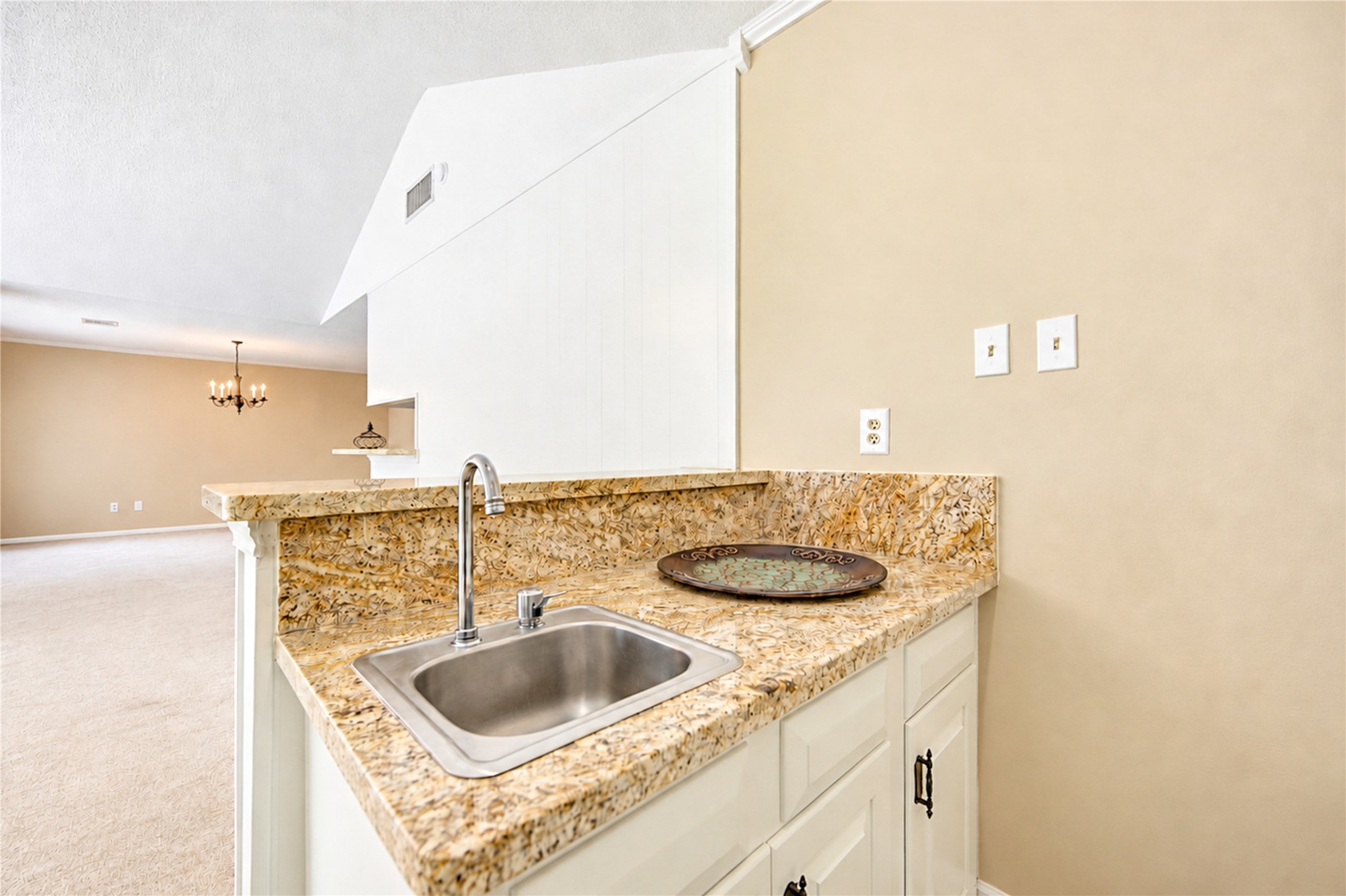 Elegant kitchen space with granite countertops and a convenient sink, featuring an open view into a spacious living area with a warm, neutral color palette.