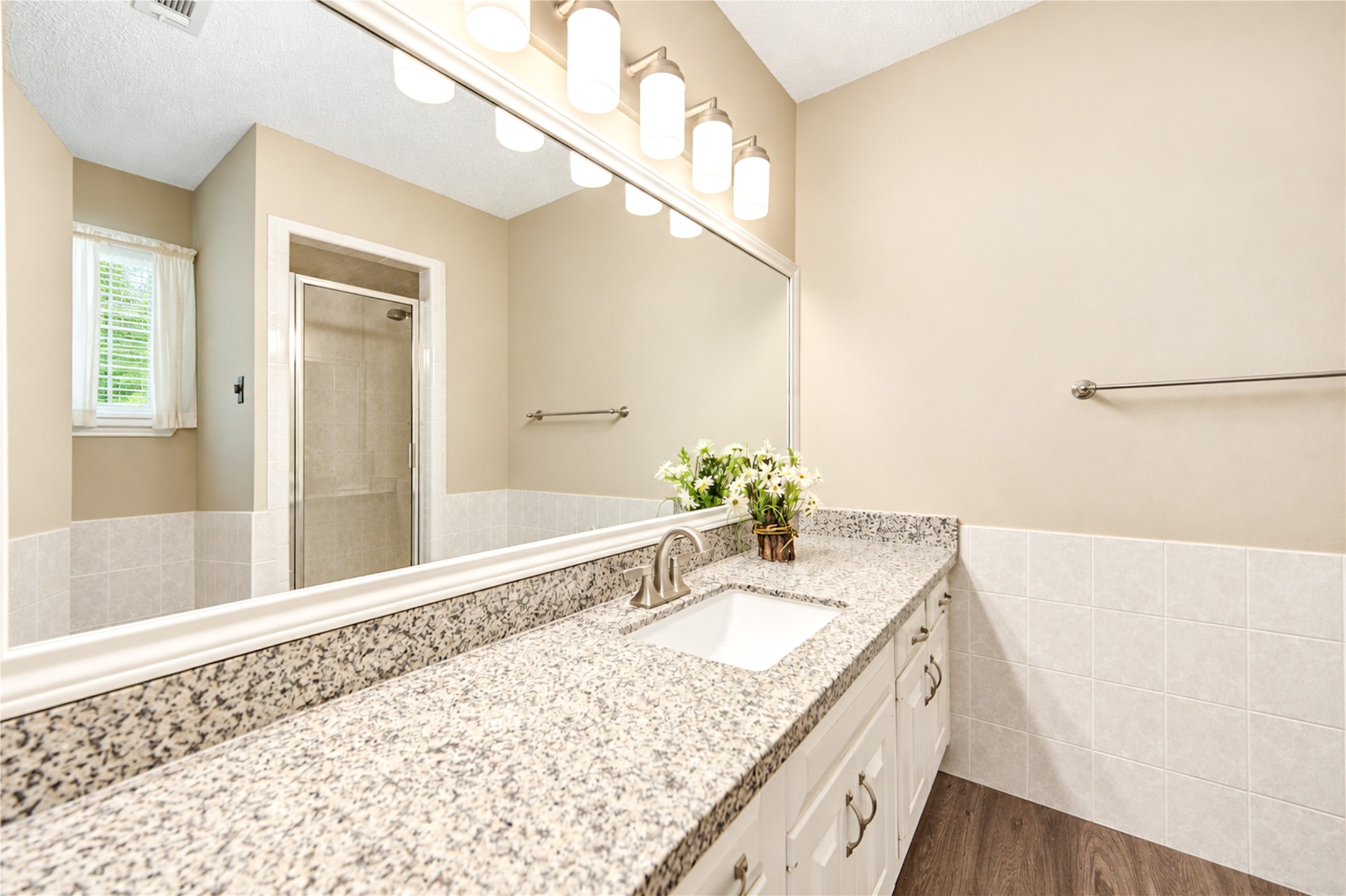 Elegant master bathroom featuring a sleek granite countertop, large mirror, and a glass-enclosed shower, complemented by warm lighting and neutral tones.