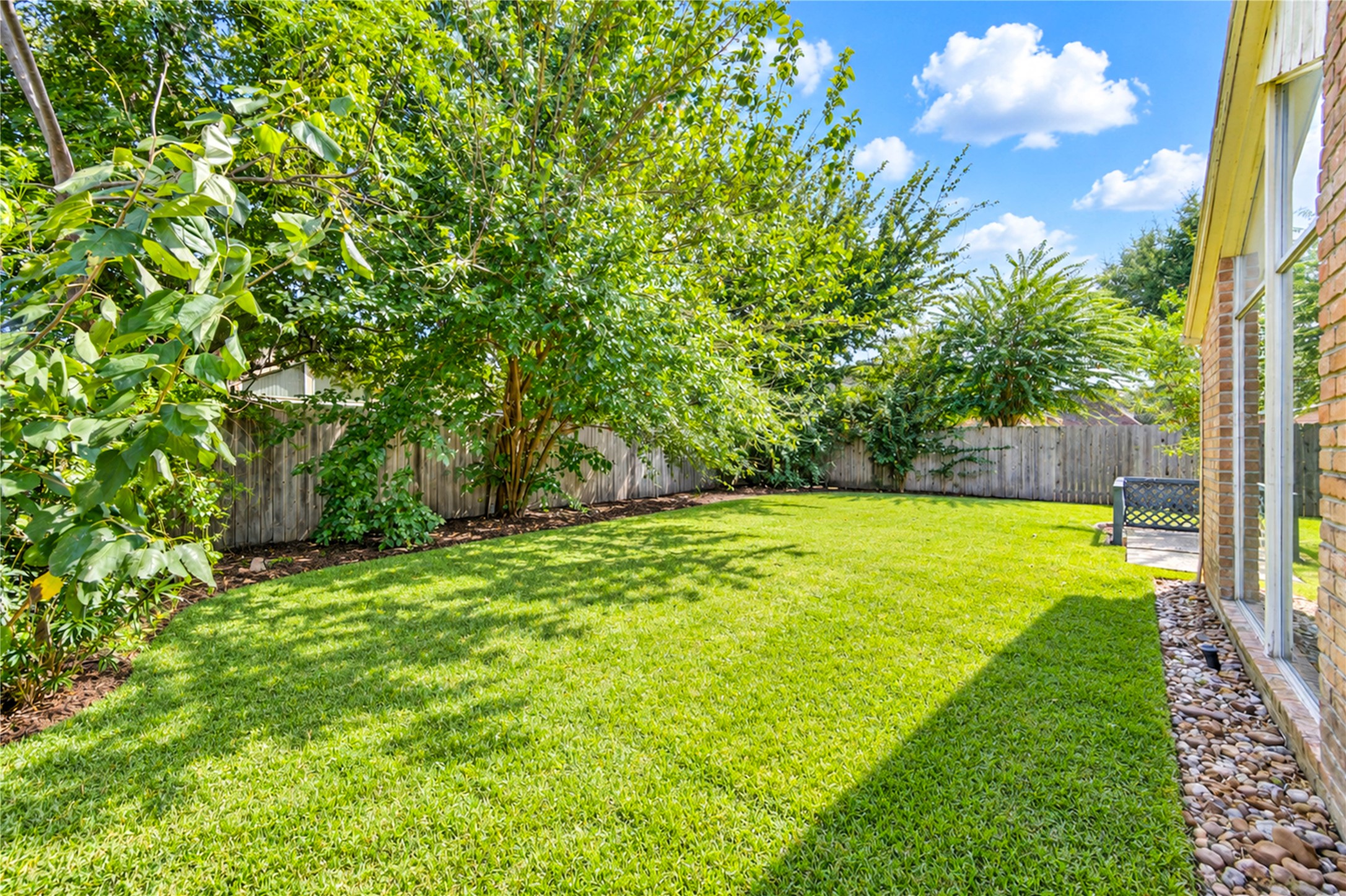 Expansive backyard with lush green lawn, mature trees for shade, and a privacy fence, perfect for outdoor activities and relaxation.