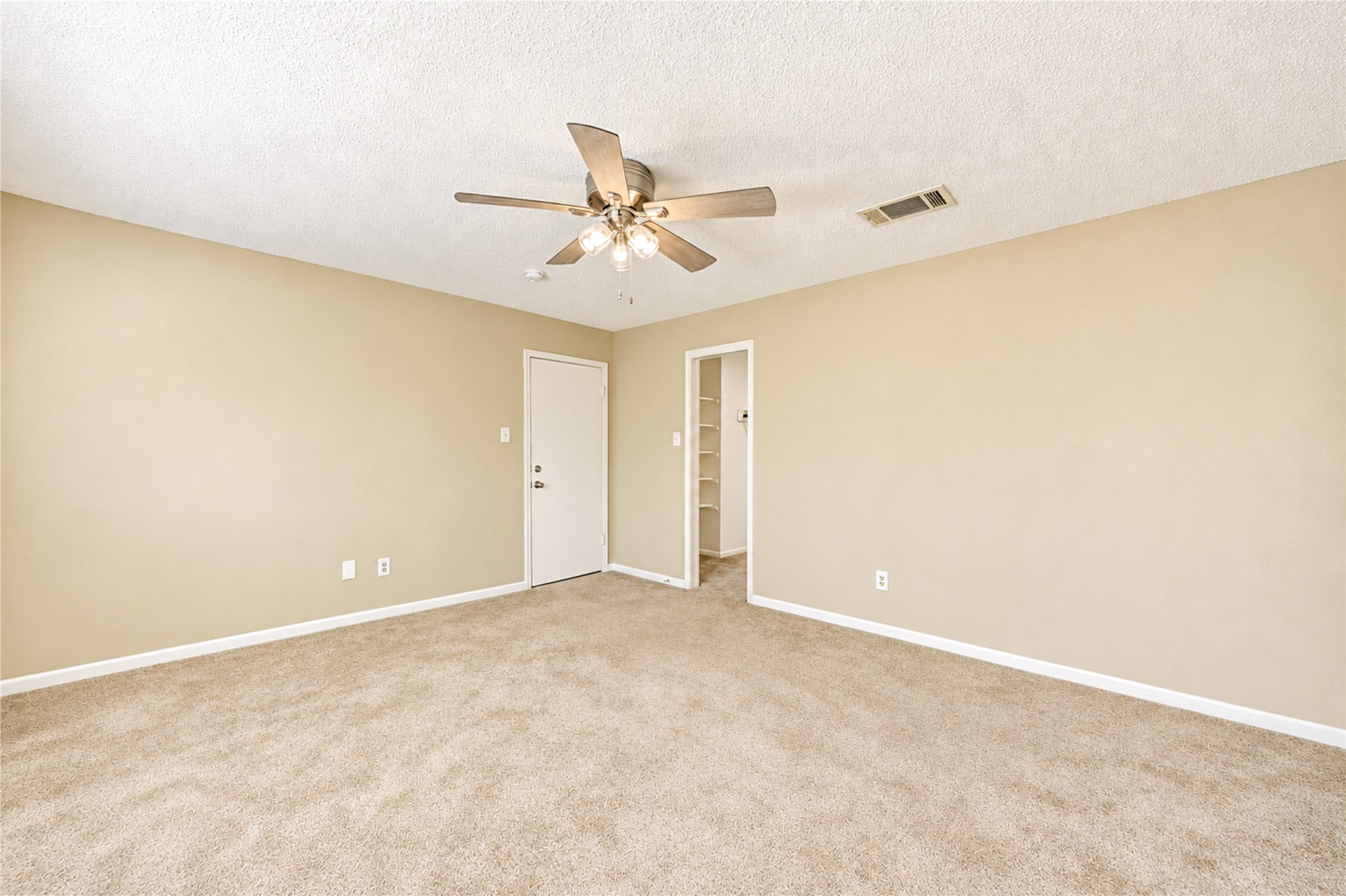 Spacious bedroom featuring plush carpet, neutral walls, a ceiling fan for comfort, and access to a walk-in closet.