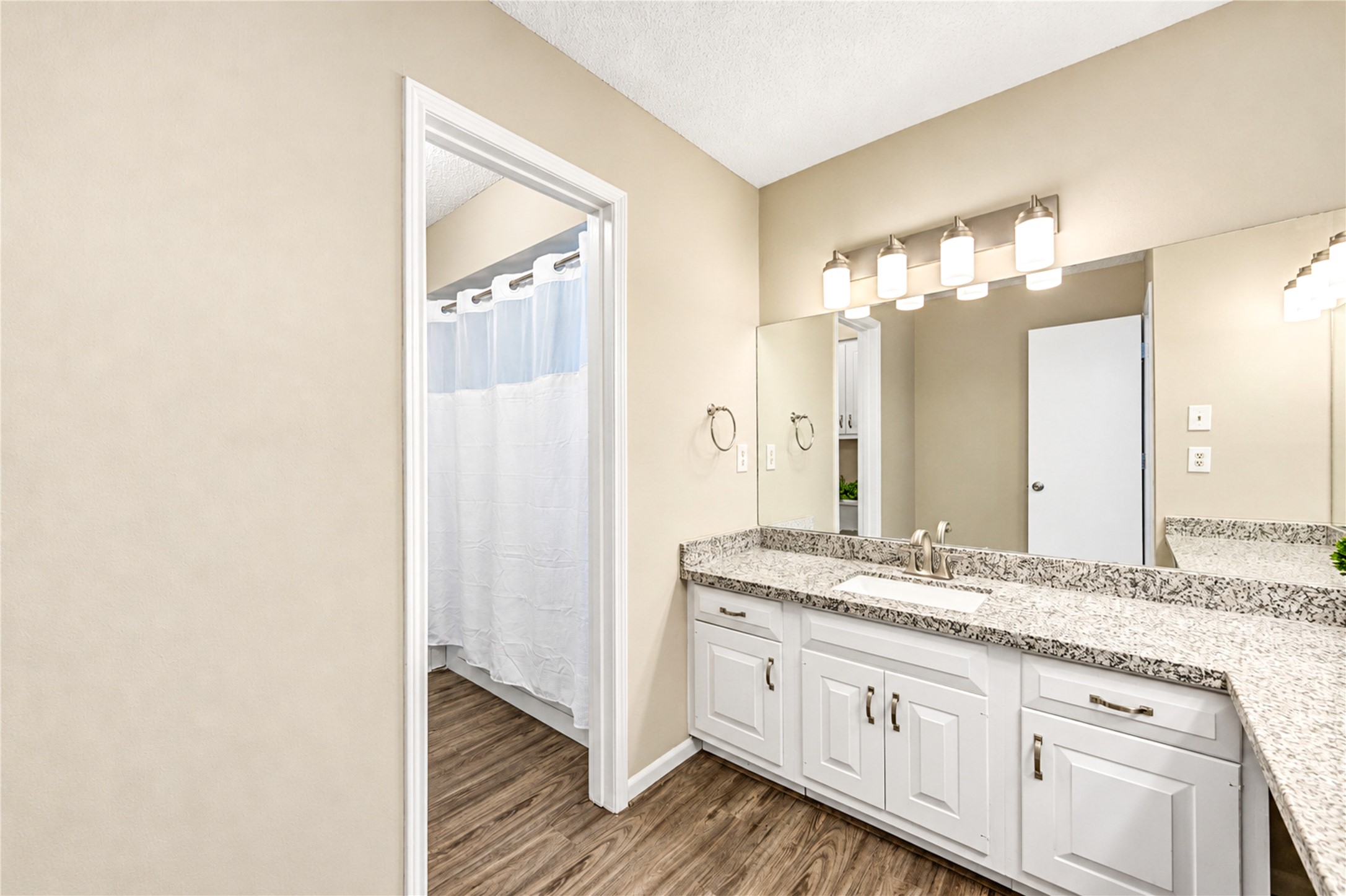 Bright and inviting bathroom featuring a stylish double vanity with granite countertops, elegant lighting, and sleek hardwood flooring.