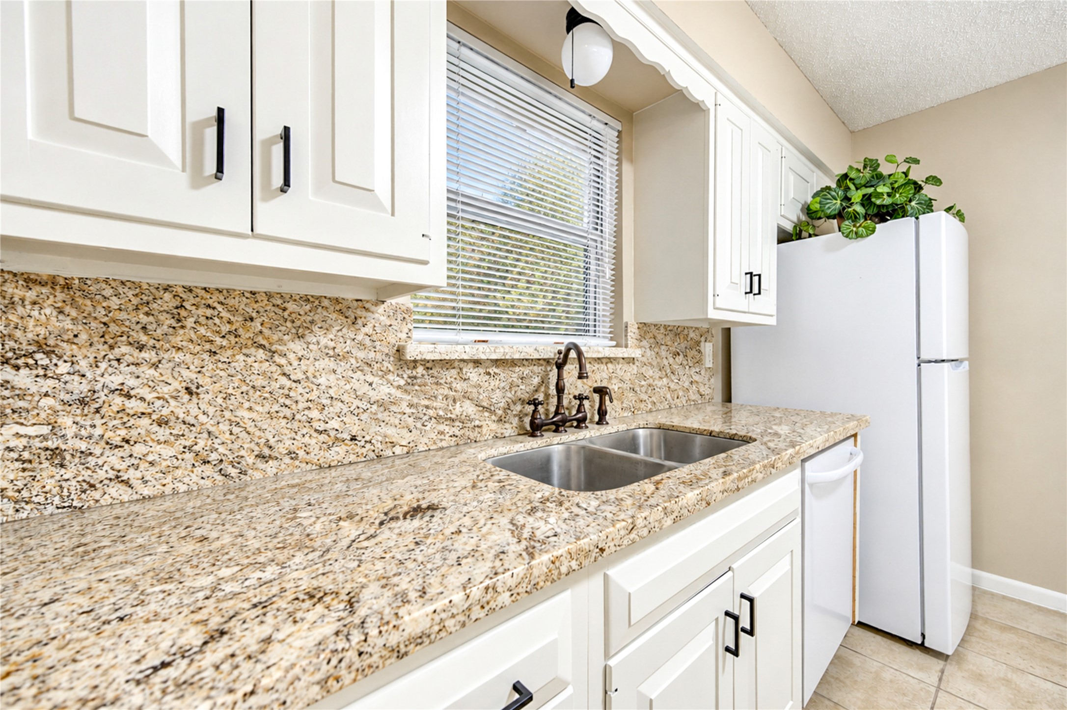 Charming kitchen with elegant granite countertops, classic white cabinetry, and a convenient double sink, complemented by natural light through a window above.