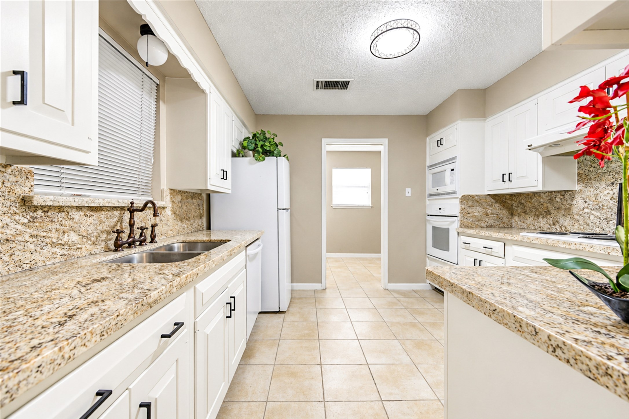 Elegant kitchen with granite countertops, white cabinetry, and modern appliances, offering ample space and a bright atmosphere.