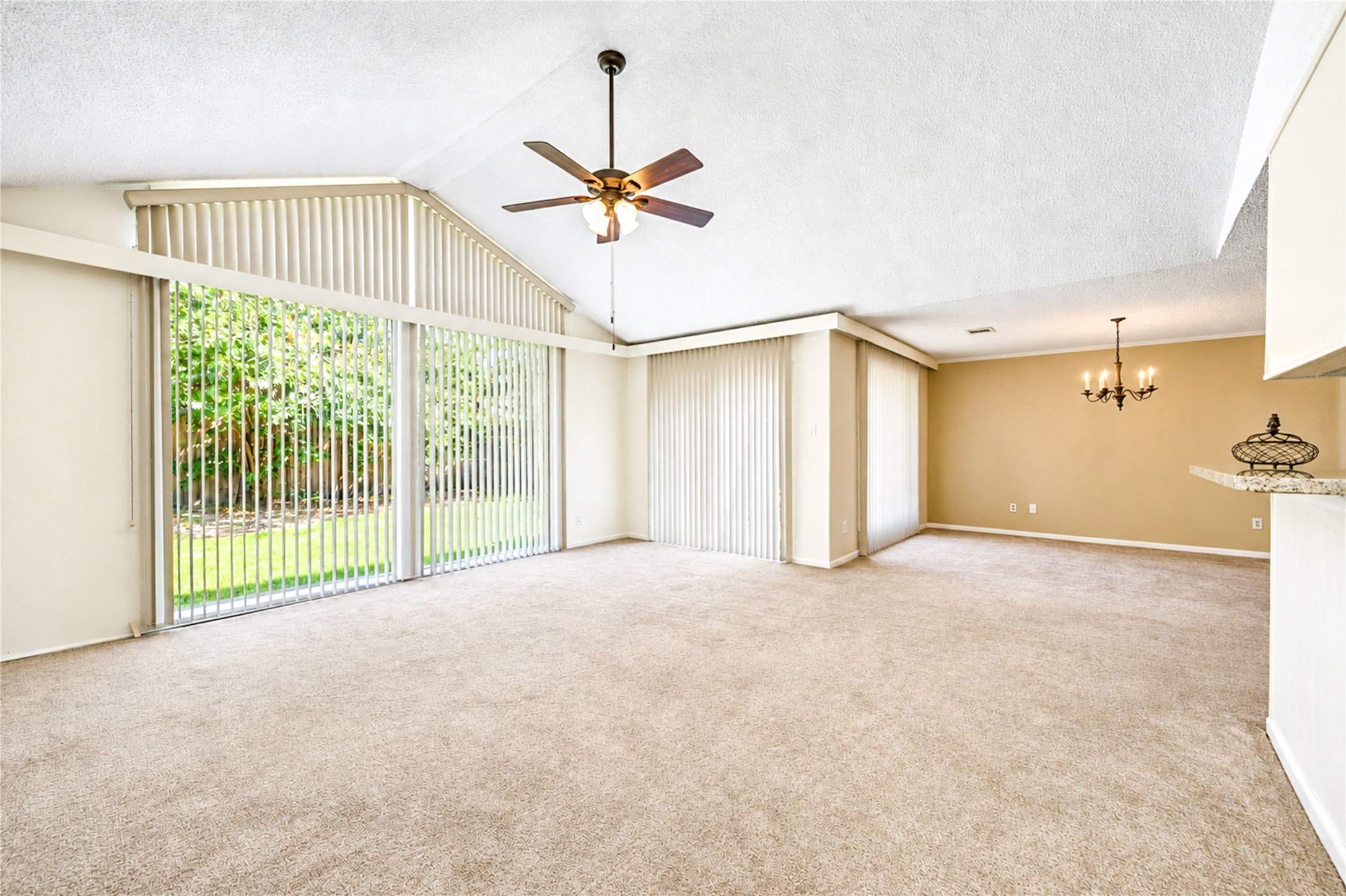 Spacious living area with vaulted ceilings and abundant natural light streaming through large windows, complemented by a stylish ceiling fan and elegant chandelier.