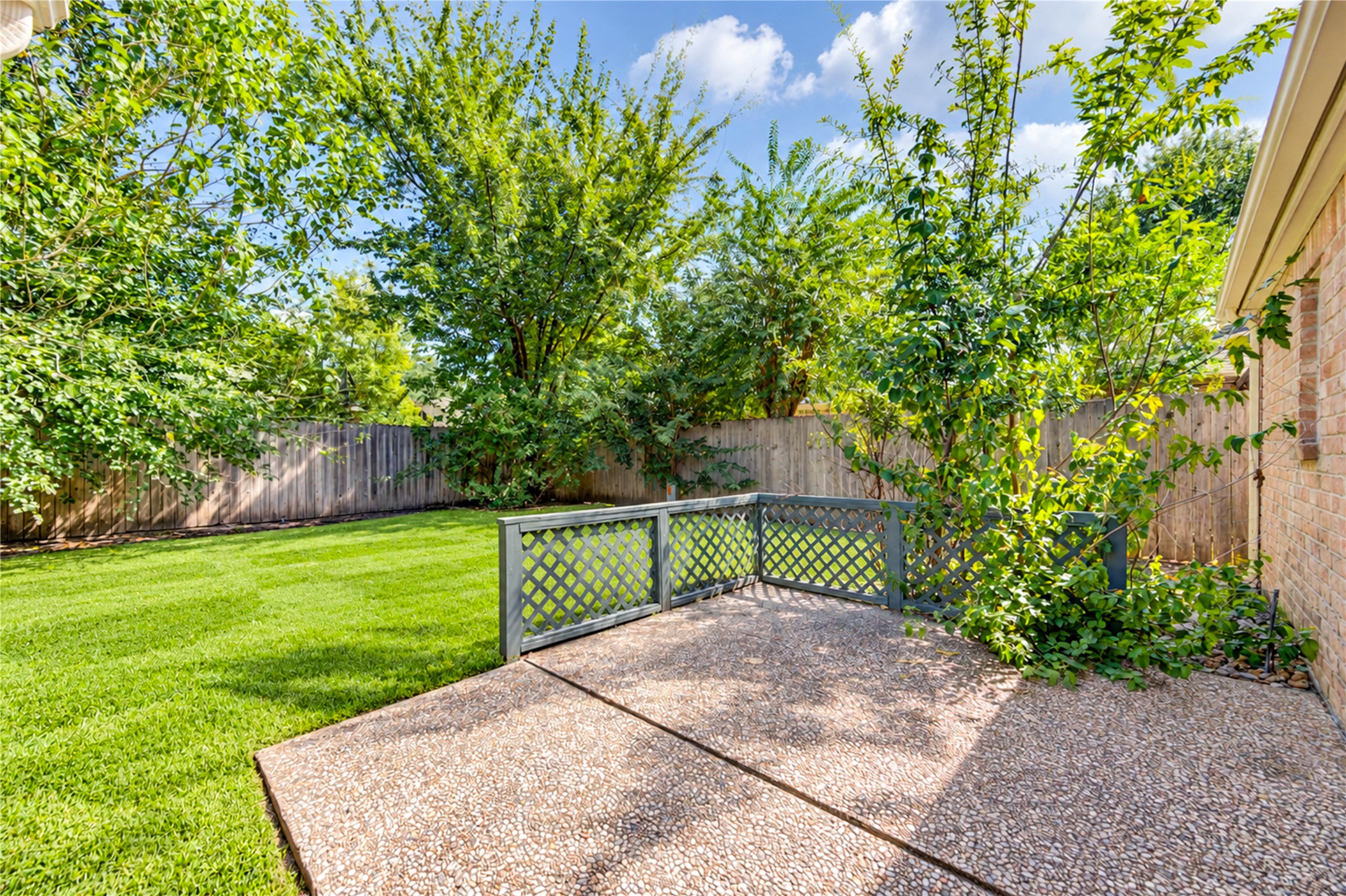 Charming backyard with lush greenery, a cozy patio area, and a privacy fence, perfect for relaxing and entertaining.