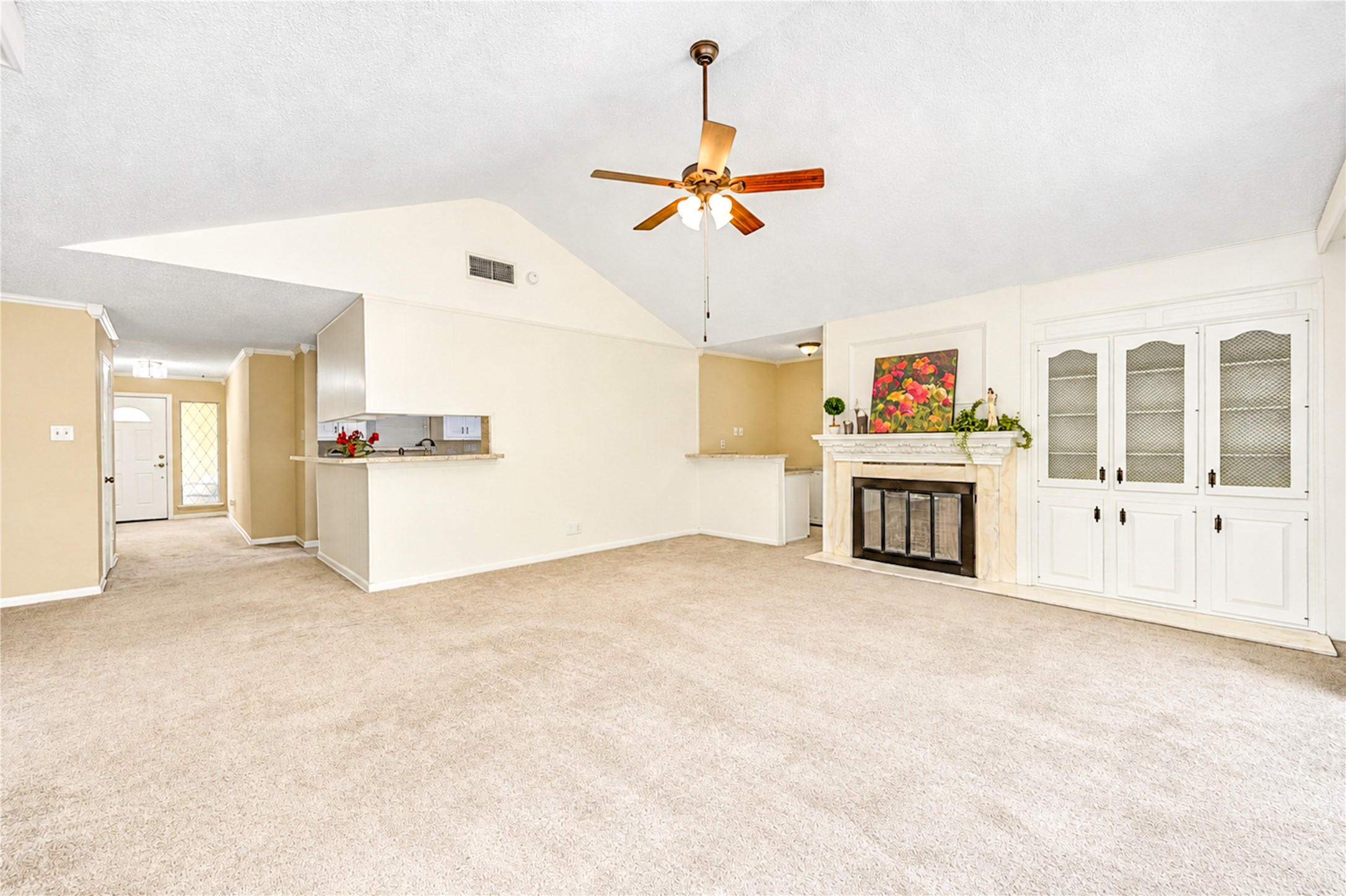 Spacious living area with vaulted ceilings, a cozy fireplace, and built-in cabinetry, complemented by an open layout leading to the kitchen.