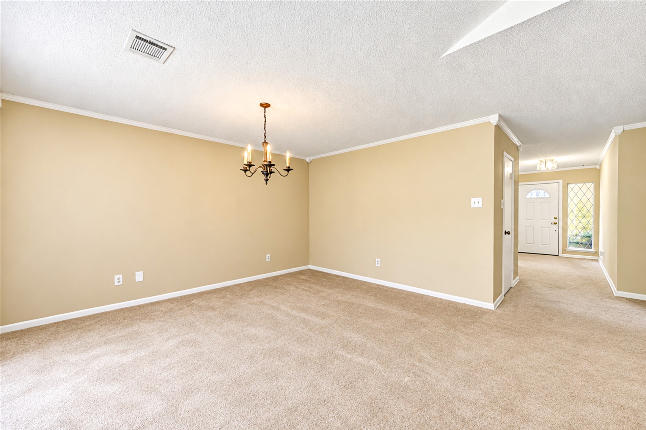 Spacious living area with plush carpeting, soft neutral tones, and elegant crown molding, enhanced by a classic chandelier and a welcoming entryway.