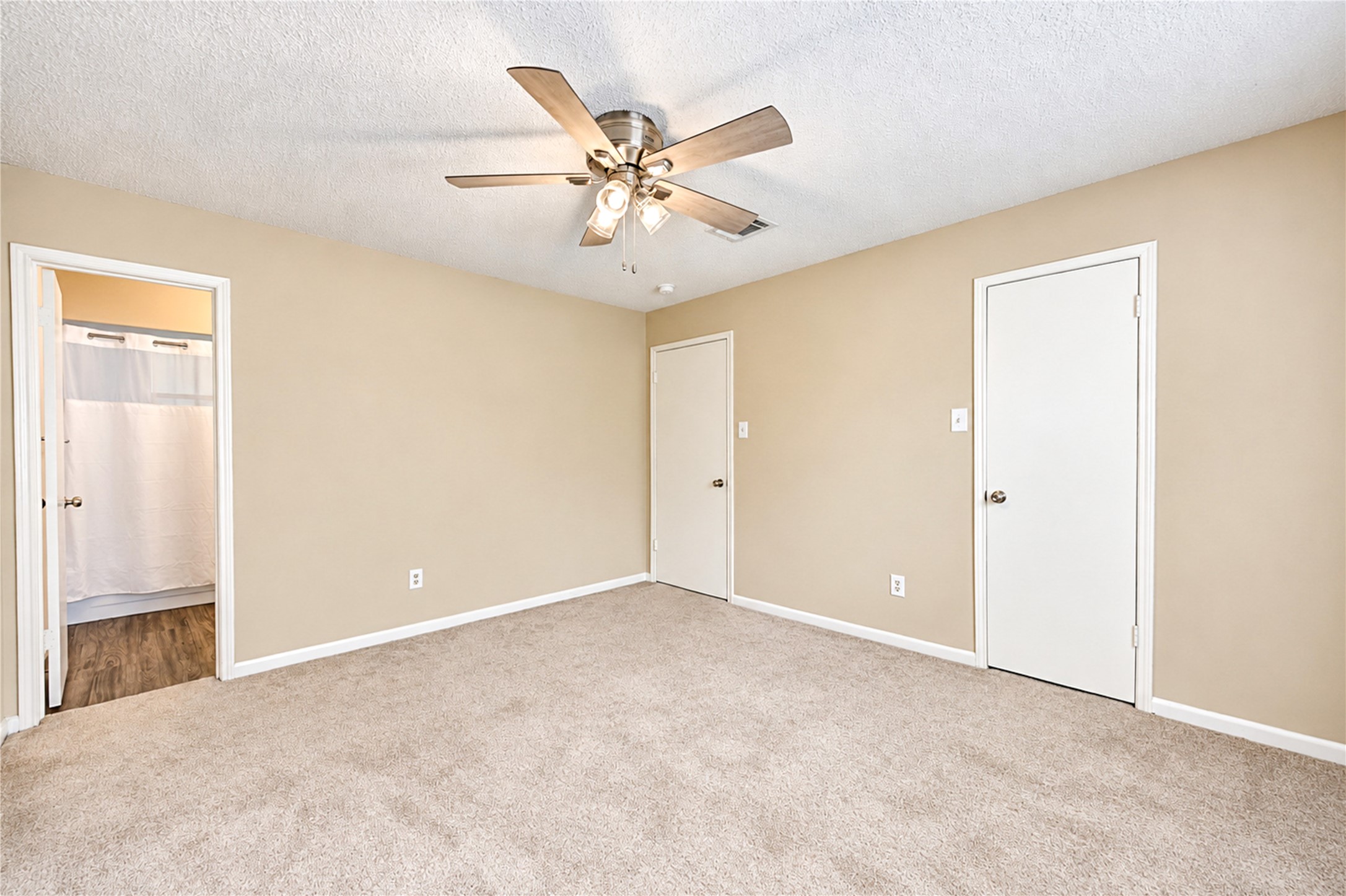 Spacious bedroom featuring soft carpet, a ceiling fan, and access to an en-suite bathroom with modern flooring.