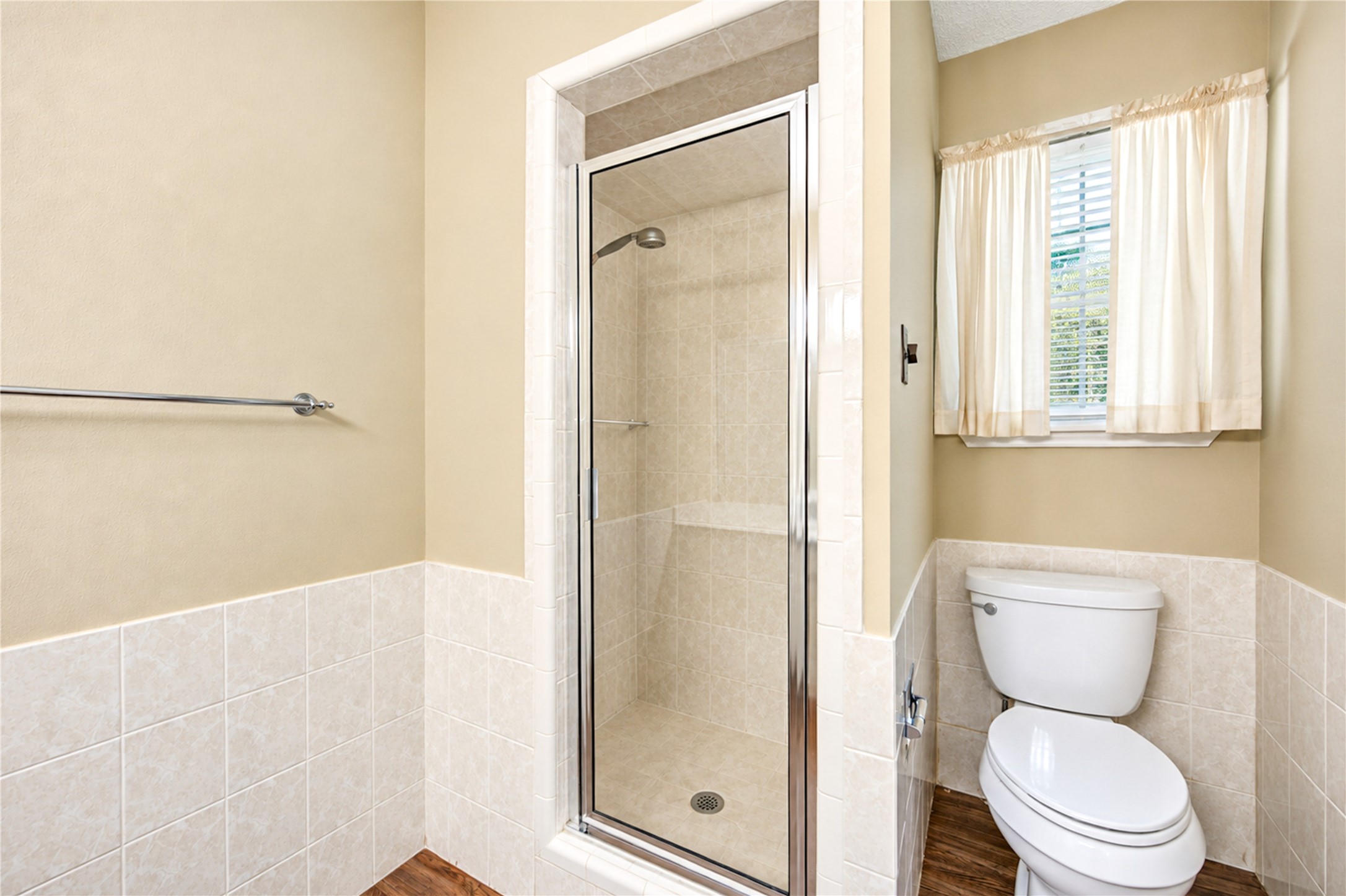 Bright bathroom featuring a tiled walk-in shower, modern fixtures, and natural light from a window with soft curtains.