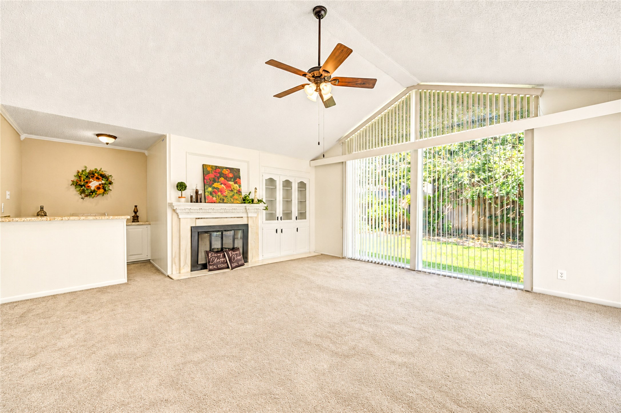 Spacious living room with vaulted ceilings, a cozy fireplace, and expansive windows offering abundant natural light and views of the lush backyard.