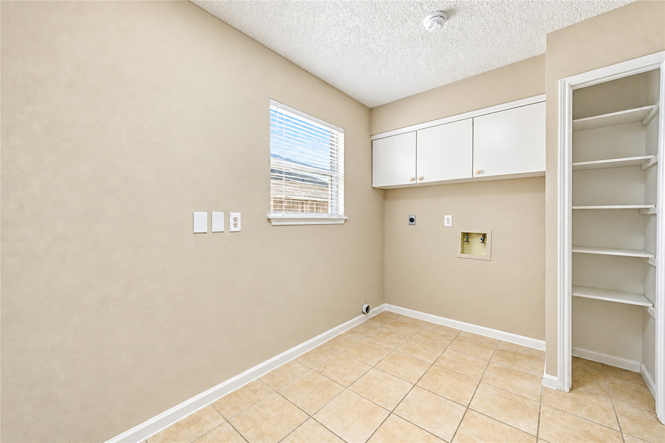 Spacious laundry room with tile flooring, built-in shelving, and ample natural light from a large window.