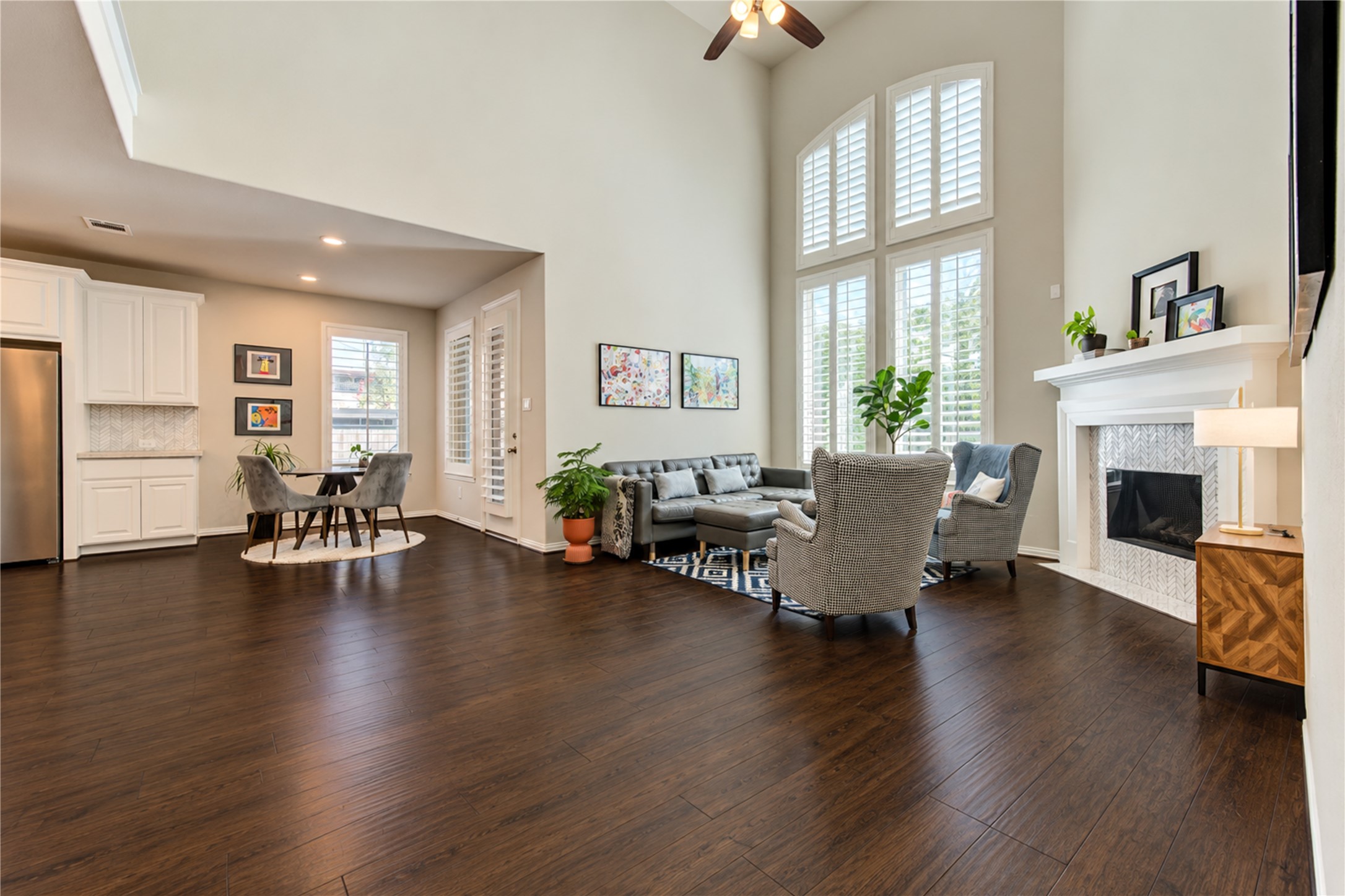 The dramatic double-height ceiling creates a grand, airy feel in the living room, complemented by a tall gas fireplace with a stylish tile surround that serves as a striking focal point.