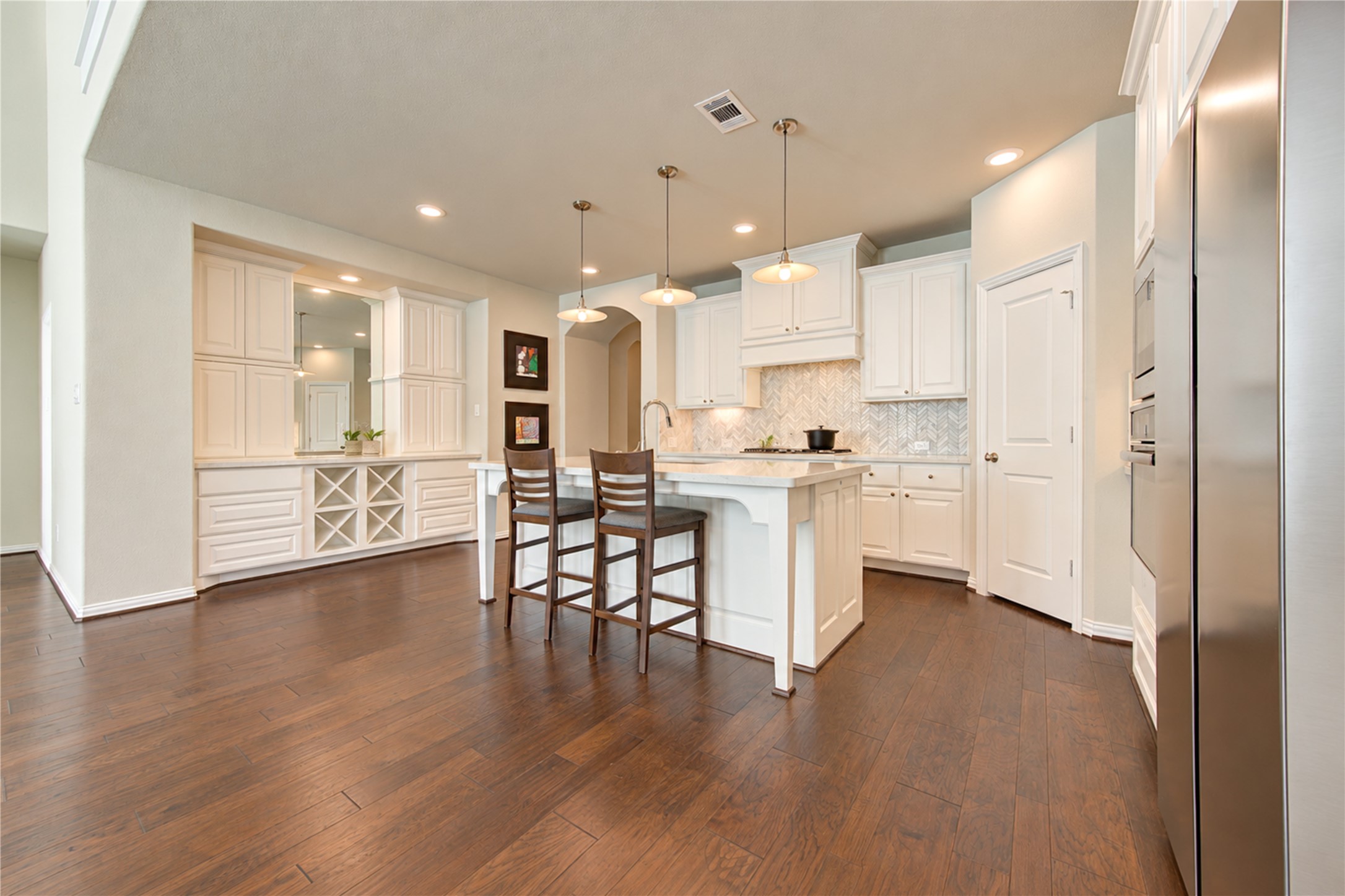 To the left of the kitchen, a convenient dry bar offers additional cabinetry and storage, while a large mirrored backsplash reflects the homes abundant natural light, enhancing the bright and open feel of the space.