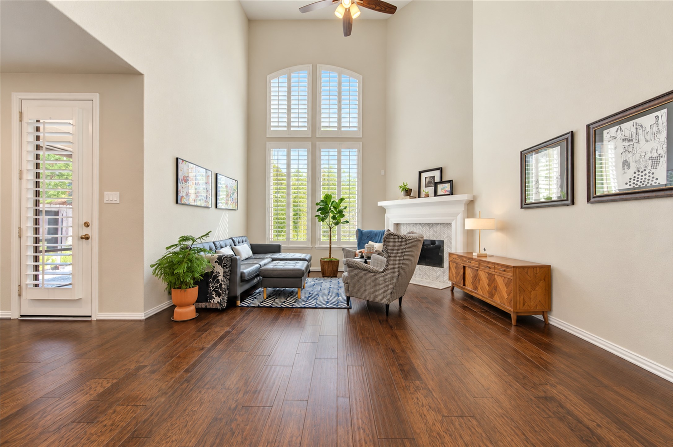 The dramatic double-height ceiling creates a grand, airy feel in the living room, complemented by a tall gas fireplace with a stylish tile surround that serves as a striking focal point.