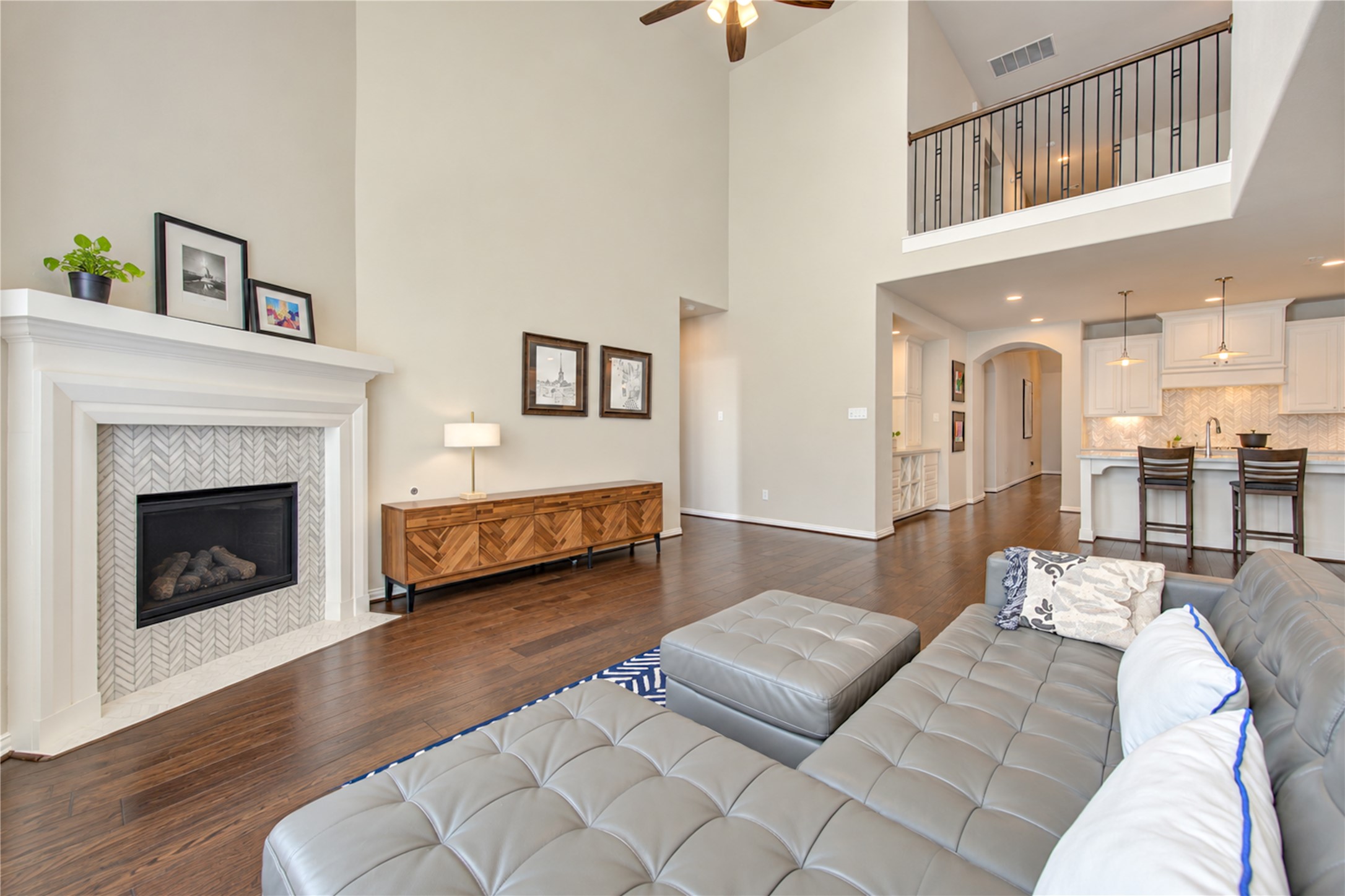 The dramatic double-height ceiling creates a grand, airy feel in the living room, complemented by a tall gas fireplace with a stylish tile surround that serves as a striking focal point.