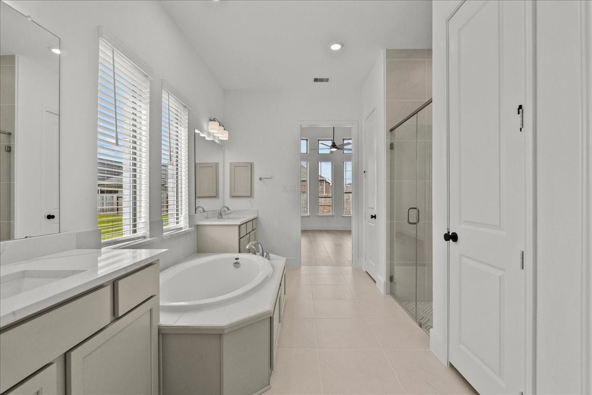 Spa-like en-suite bath with dual vanities, a walk-in shower, soaking tub, and large walk-in closet