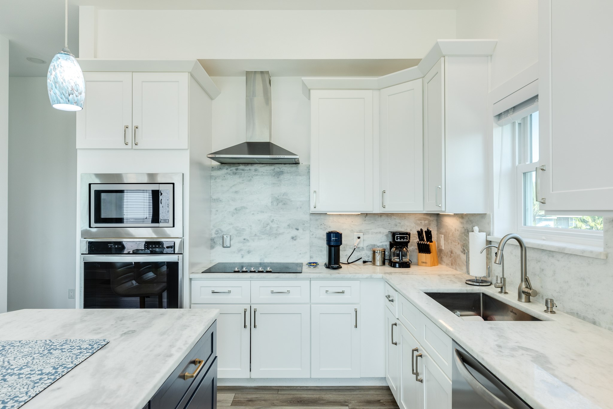 Kitchen detail view. Electric 5 burner cooktop with vent hood, separate electric oven with cabinet level microwave. Quartz countertops and backsplash accentuate the sleek finish of this kitchen.