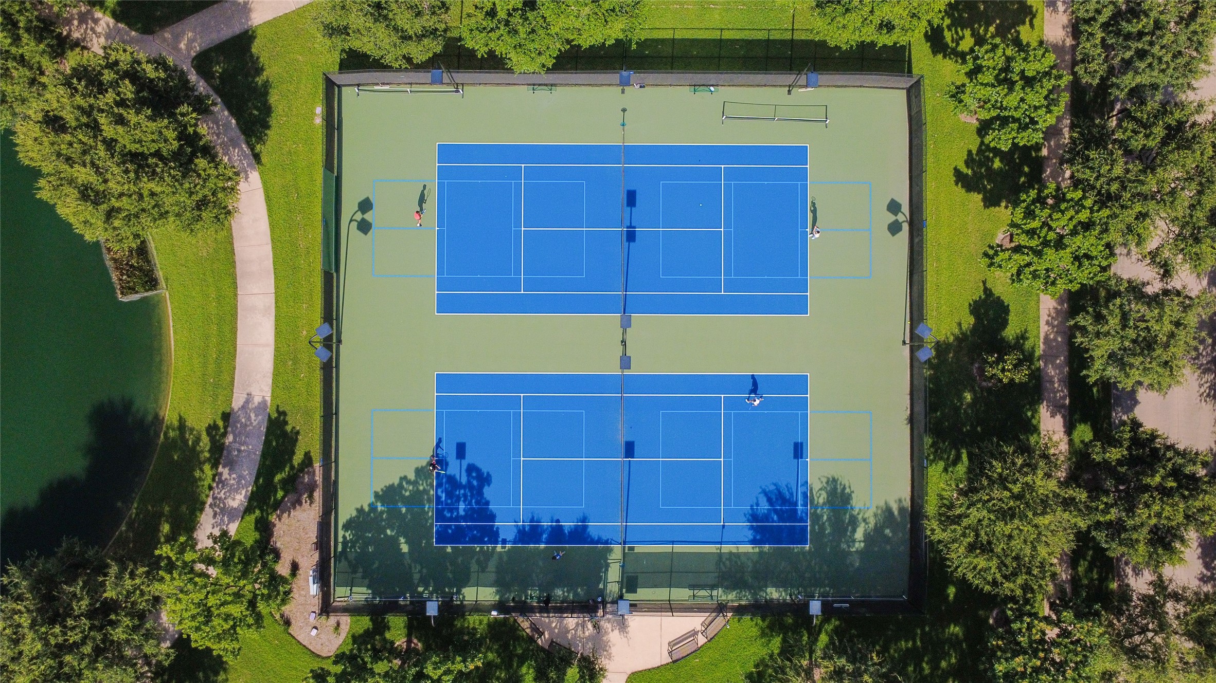 This aerial photo showcases two well-maintained tennis courts surrounded by lush greenery and walking paths, ideal for an active lifestyle in a serene setting.