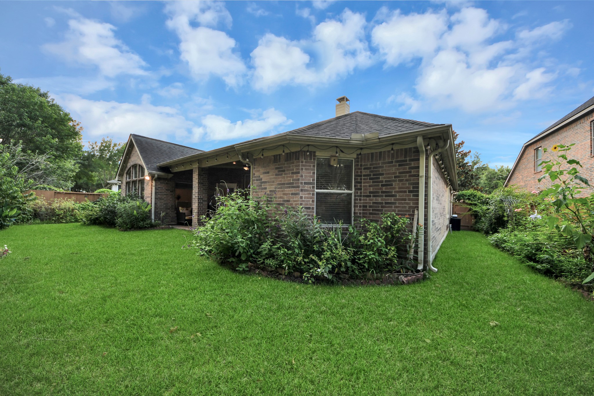 Charming brick home with a spacious, well-maintained backyard. Features a covered patio area, perfect for outdoor relaxation. Lush greenery surrounds the property, offering privacy and a serene atmosphere.
