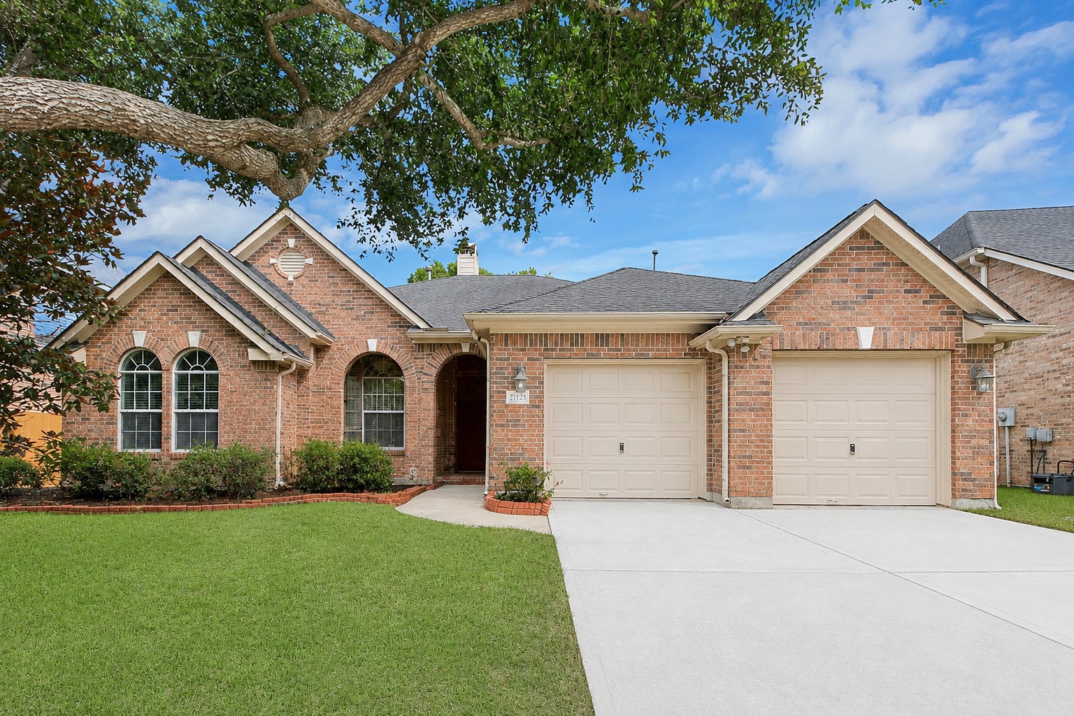 This charming brick home features a well-maintained lawn, two-car garage, and inviting arched windows. The mature tree offers shade and enhances curb appeal. Ideal for families seeking a cozy and welcoming environment.