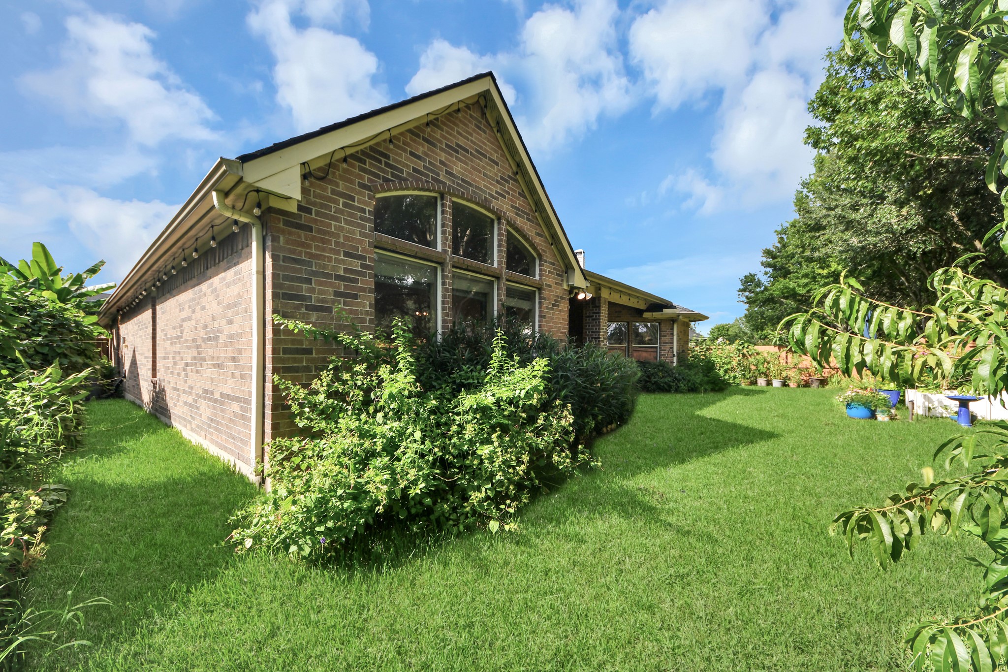 This photo showcases a charming brick home with a lush, green backyard. The house features large windows and a well-maintained lawn surrounded by mature trees and shrubs, offering a serene and private outdoor space.