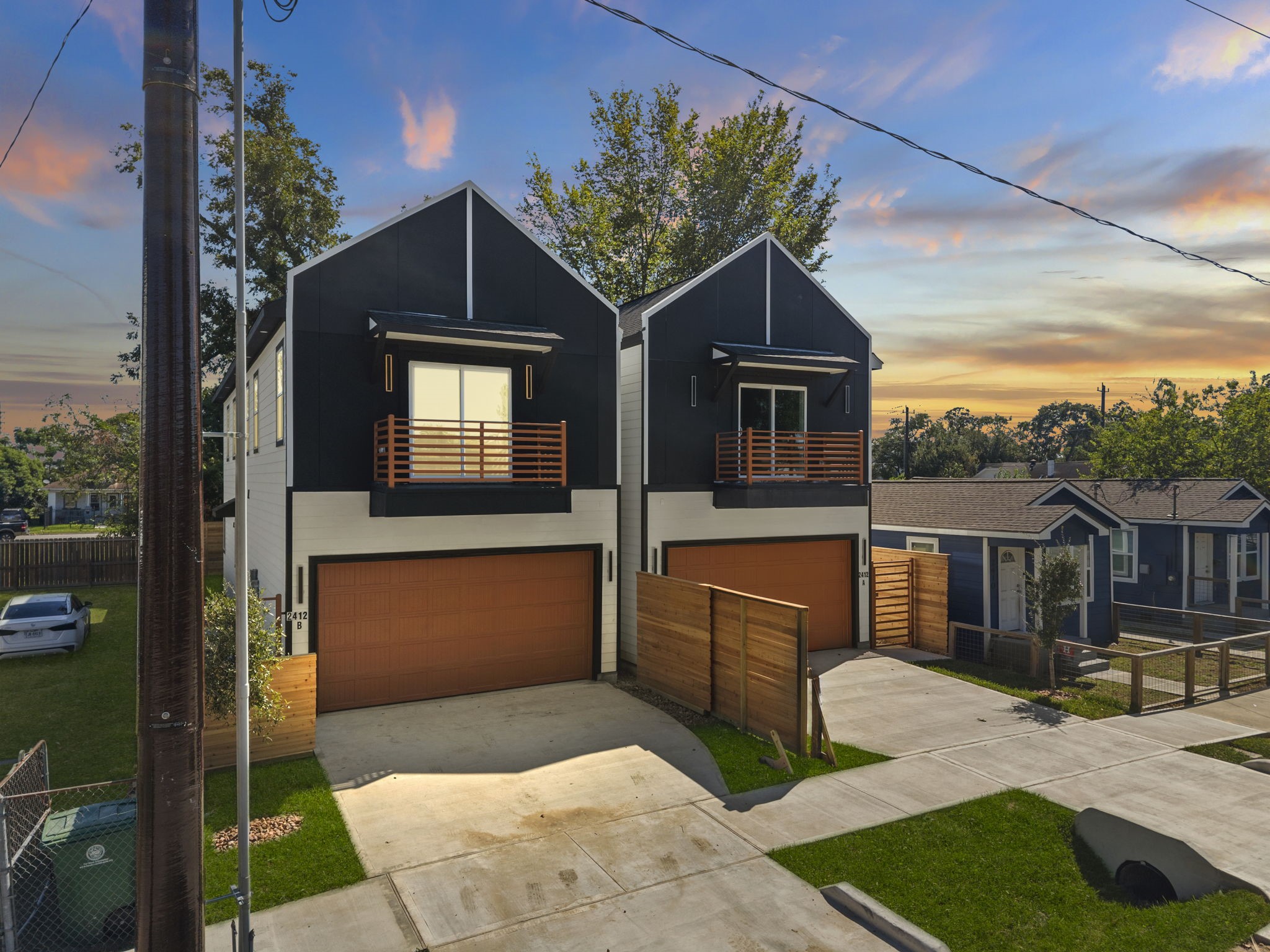 This striking two-story home features sharp gabled architecture and sleek modern paneling. Private upper balconies extend the living space outdoors, while an expansive concrete driveway and neatly landscaped yard provide generous off-street parking and excellent functional footprint.
