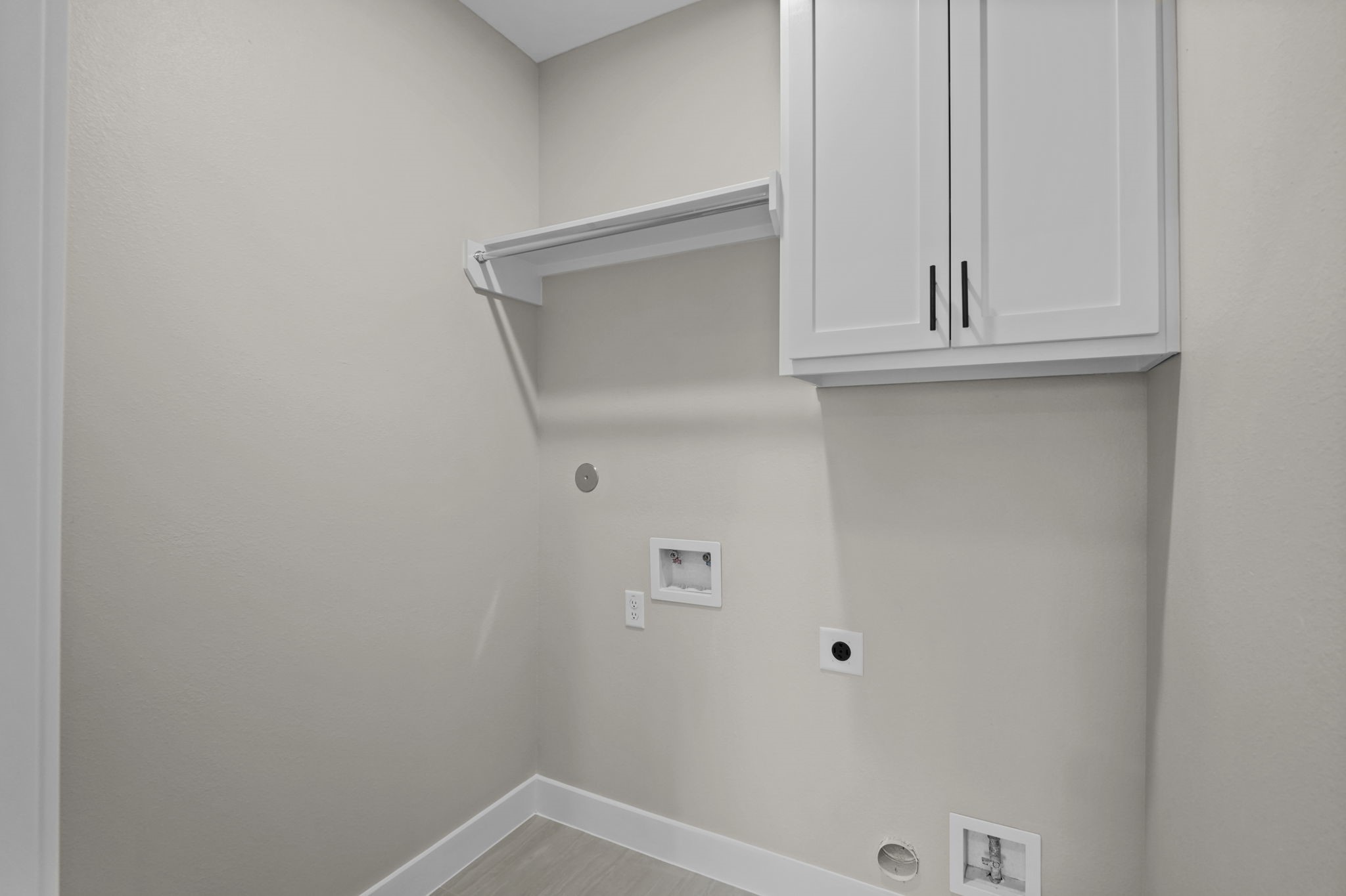 This dedicated laundry room features upper wall cabinetry and an attached hanging rod for easy organization and air-drying.