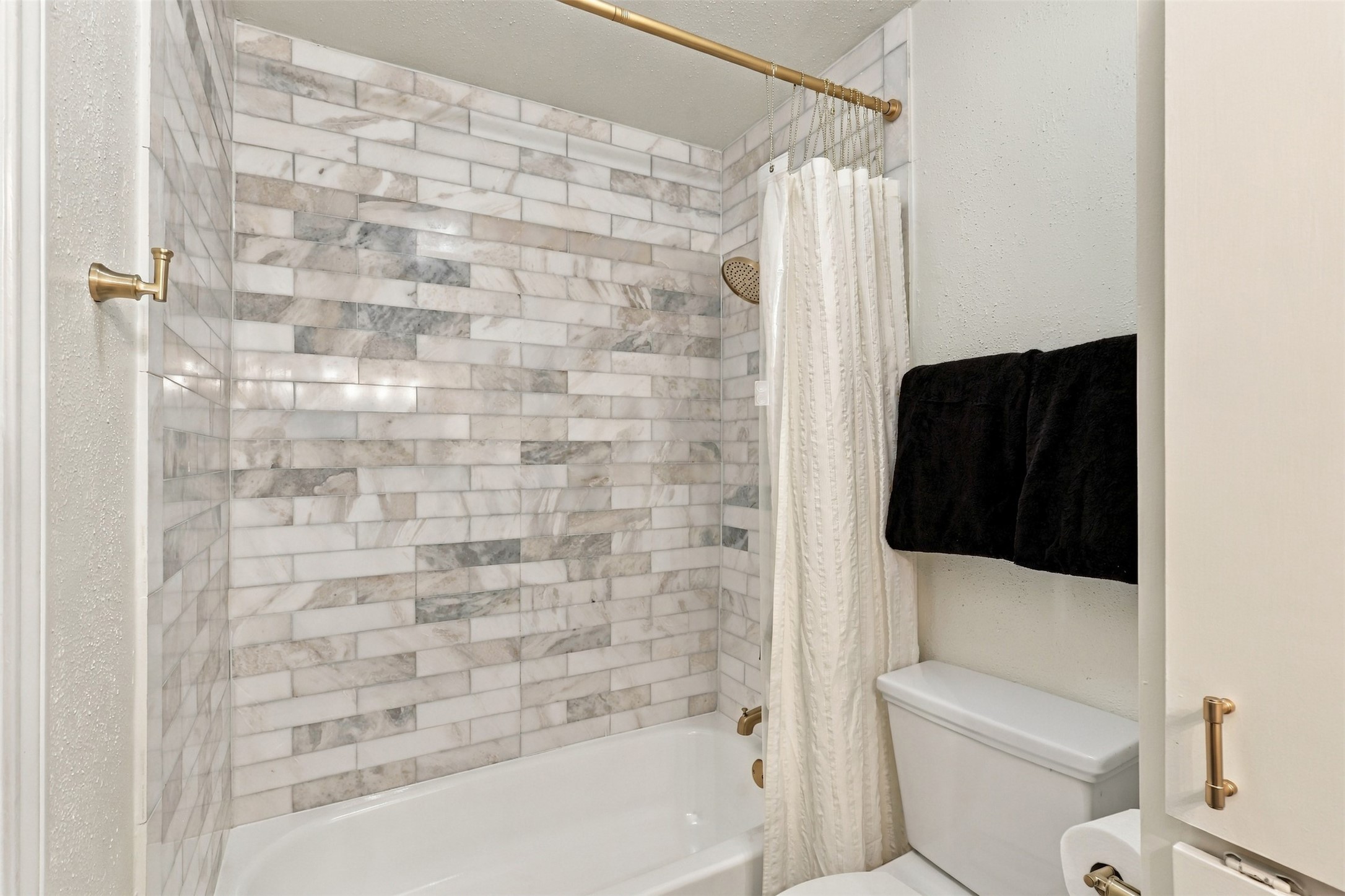 Elegant bathroom featuring a luxurious marble-tiled shower, complemented by a classic white bathtub and gold fixtures.