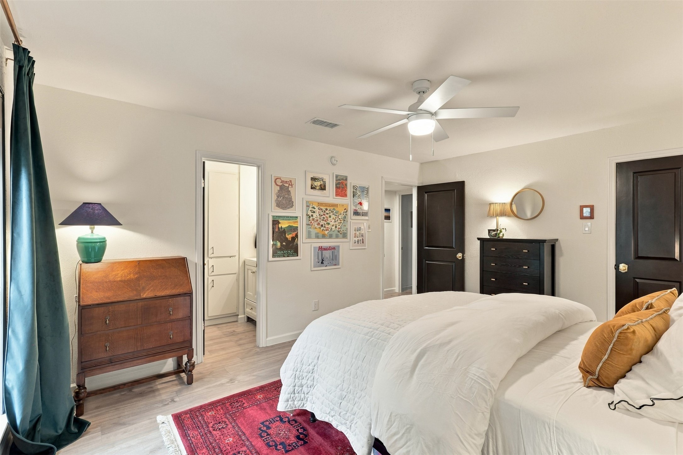 Cozy bedroom featuring a stylish ceiling fan, elegant dark wood furniture, and a vibrant red area rug. Soft lighting complements the tasteful wall art, creating a warm and inviting atmosphere.