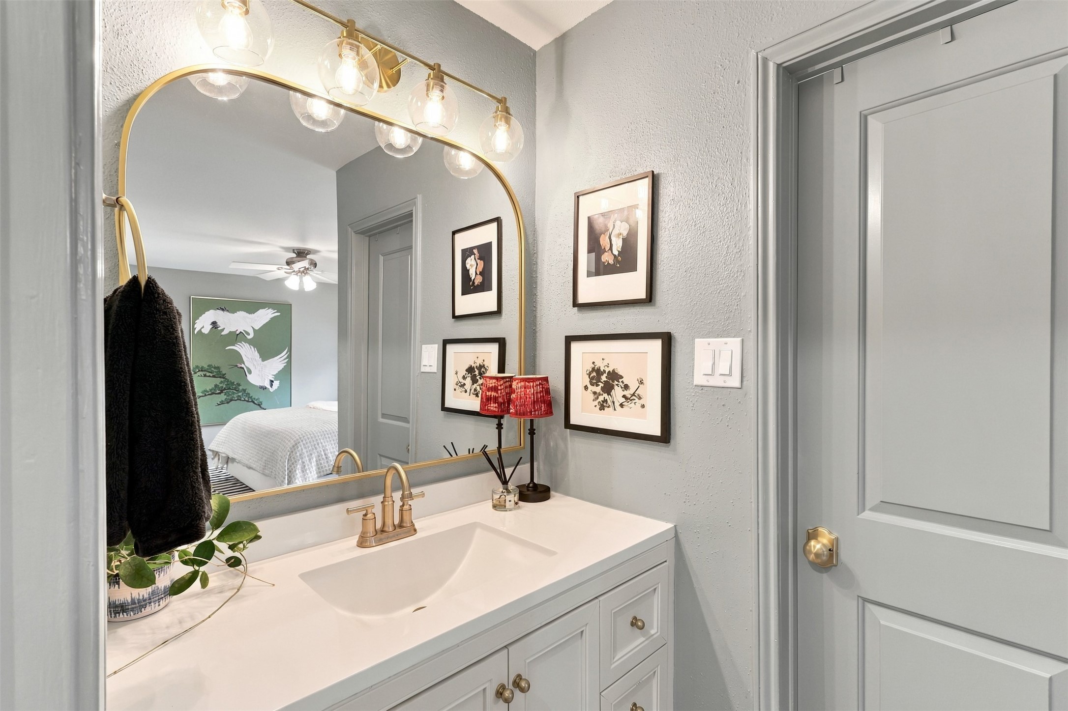 Stylish bathroom features a sleek vanity with a gold-framed mirror, elegant lighting, and tasteful artwork, providing a modern and inviting atmosphere.