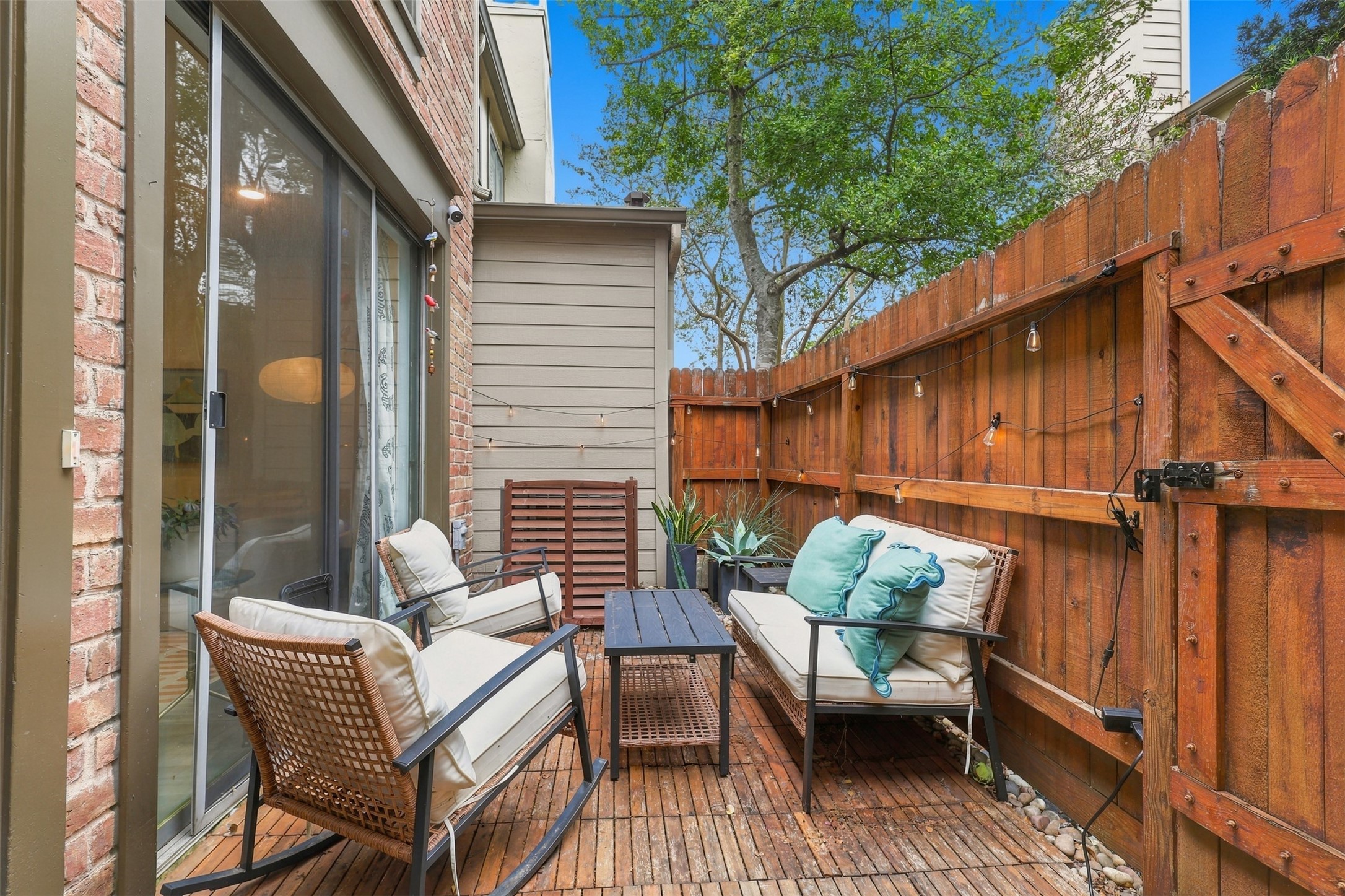 Charming patio area with cozy seating, surrounded by a wooden privacy fence and lush greenery, perfect for relaxing outdoors.