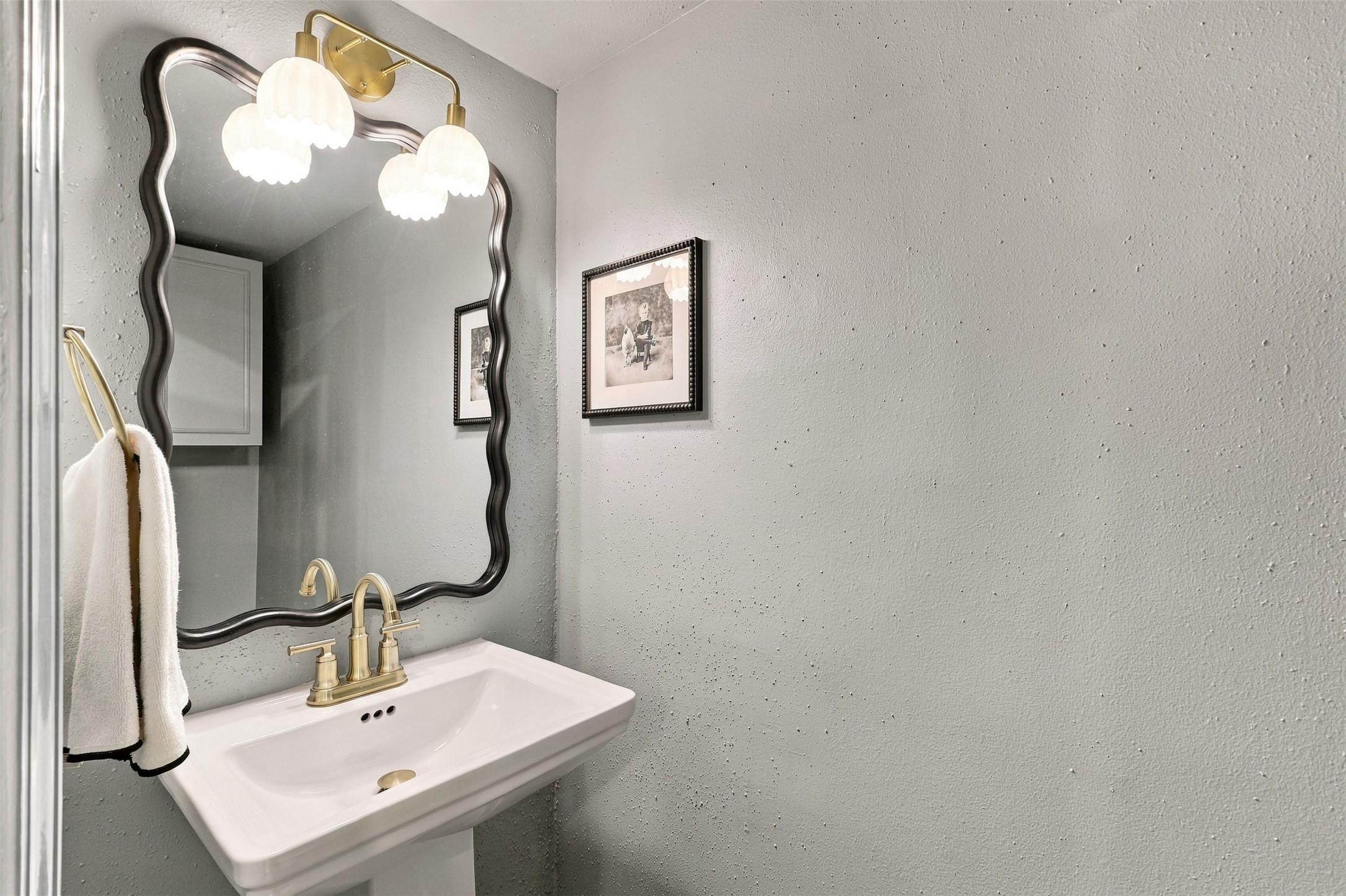 Charming powder room featuring a sleek pedestal sink, elegant gold fixtures, and a decorative mirror, complemented by soft lighting and subtle wall art.